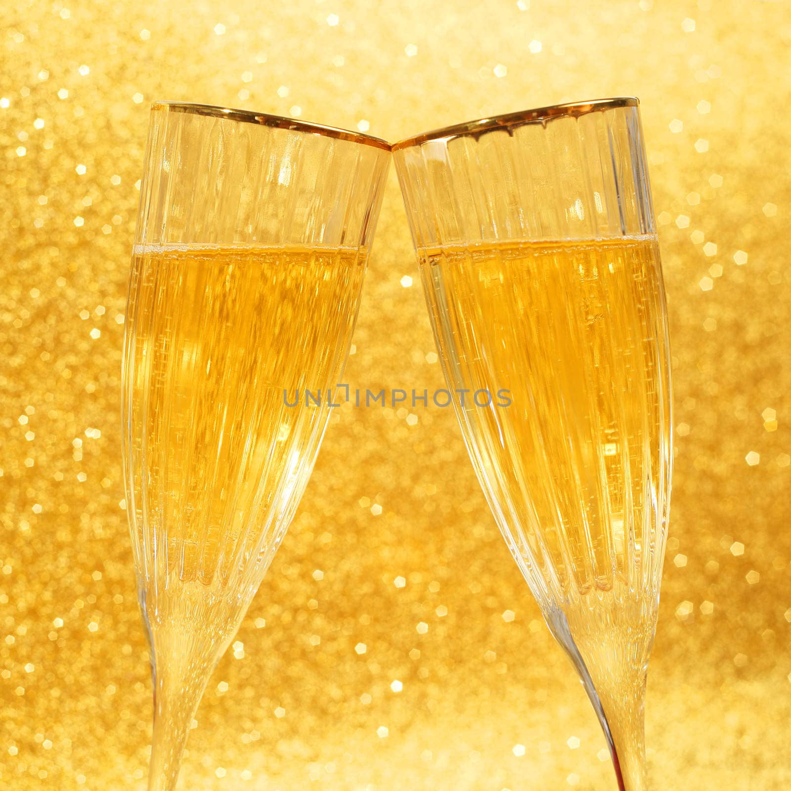 Two clinking glasses of champagne with golden glitter lights on background
