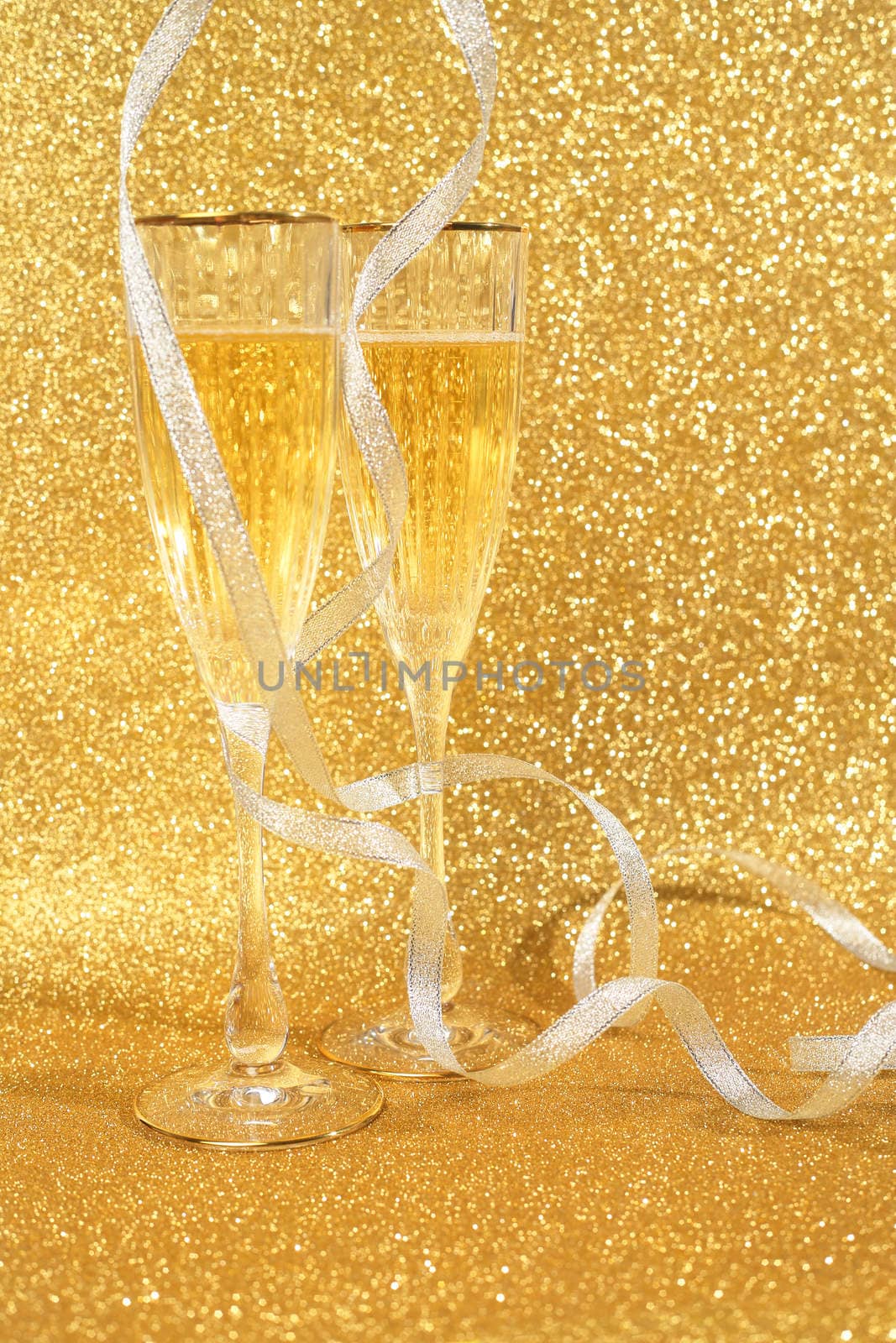 Two glasses of champagne with golden glitter lights on background