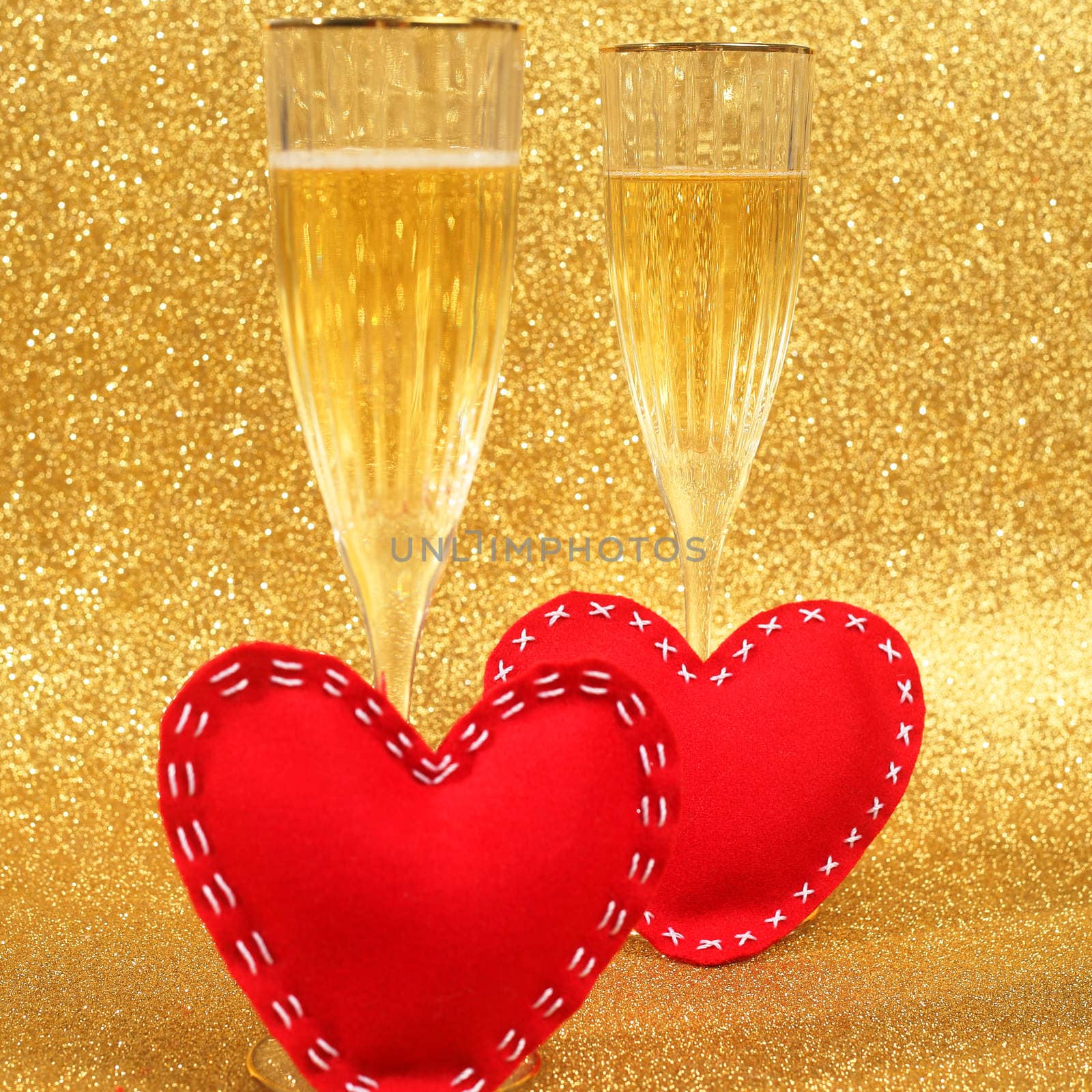 Two glasses of champagne and red hearts with golden glitter lights on background