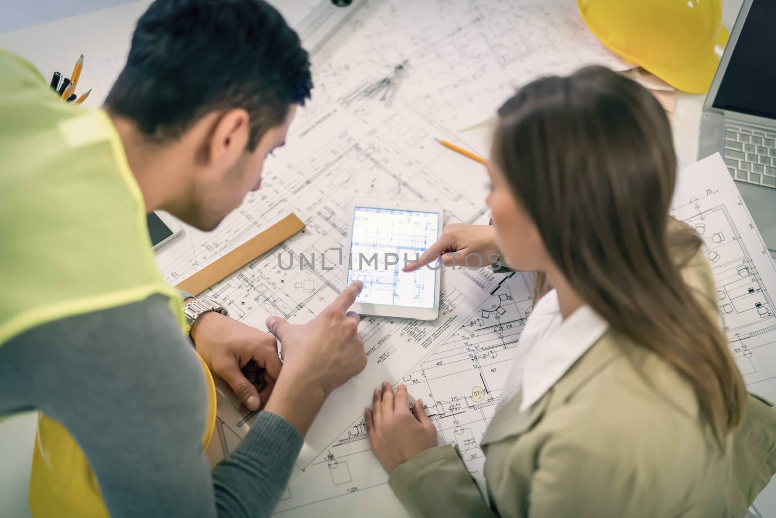 Top view of successful young architects checking the architectural plans on tablet in the office.