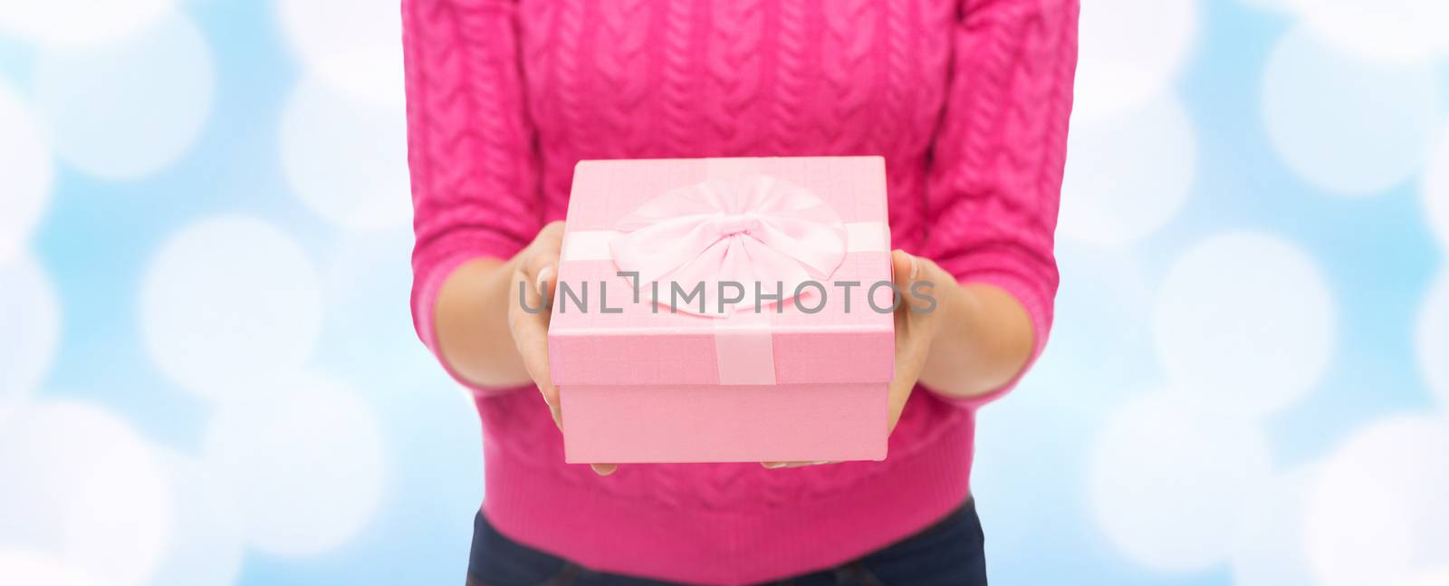 christmas, holidays and people concept - close up of woman in pink sweater holding gift box over blue lights background