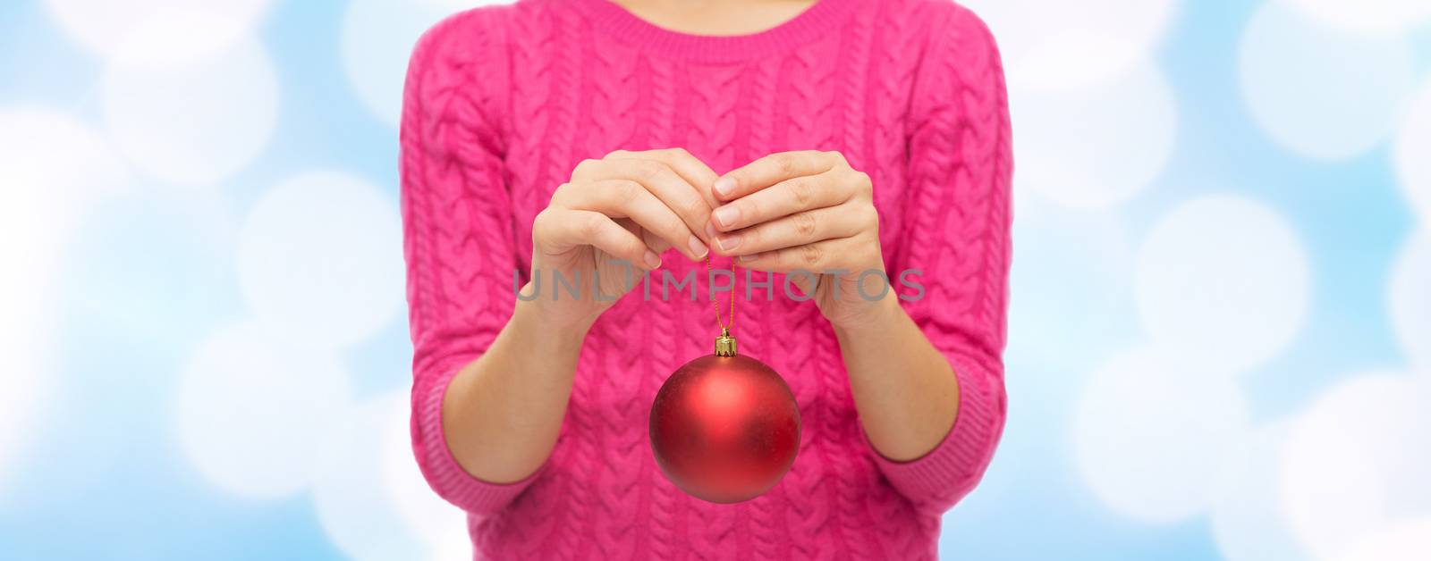 christmas, decoration, holidays and people concept - close up of woman in pink sweater holding christmas ball over blue lights background