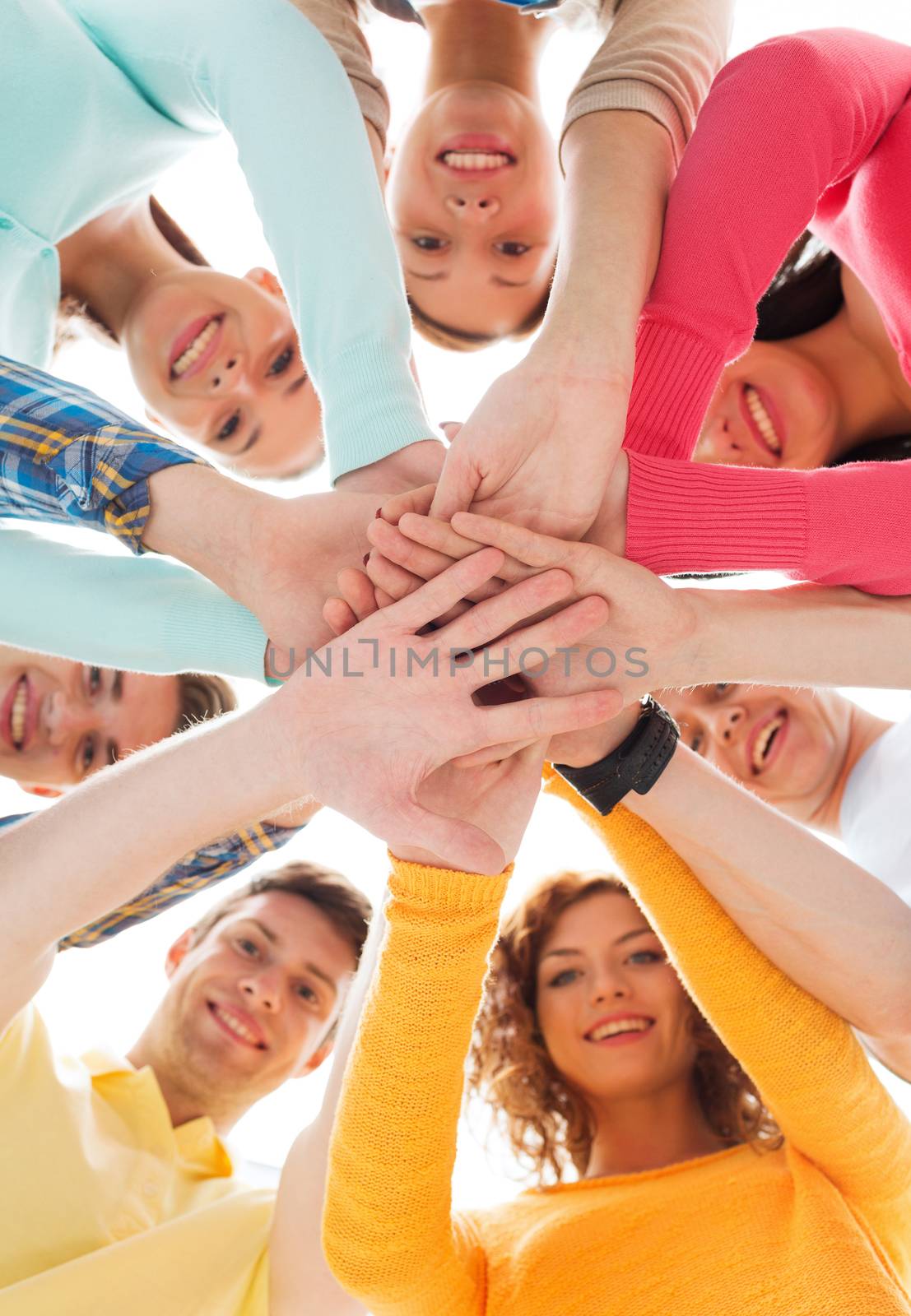 friendship, youth and people concept - group of smiling teenagers with hands on top of each other