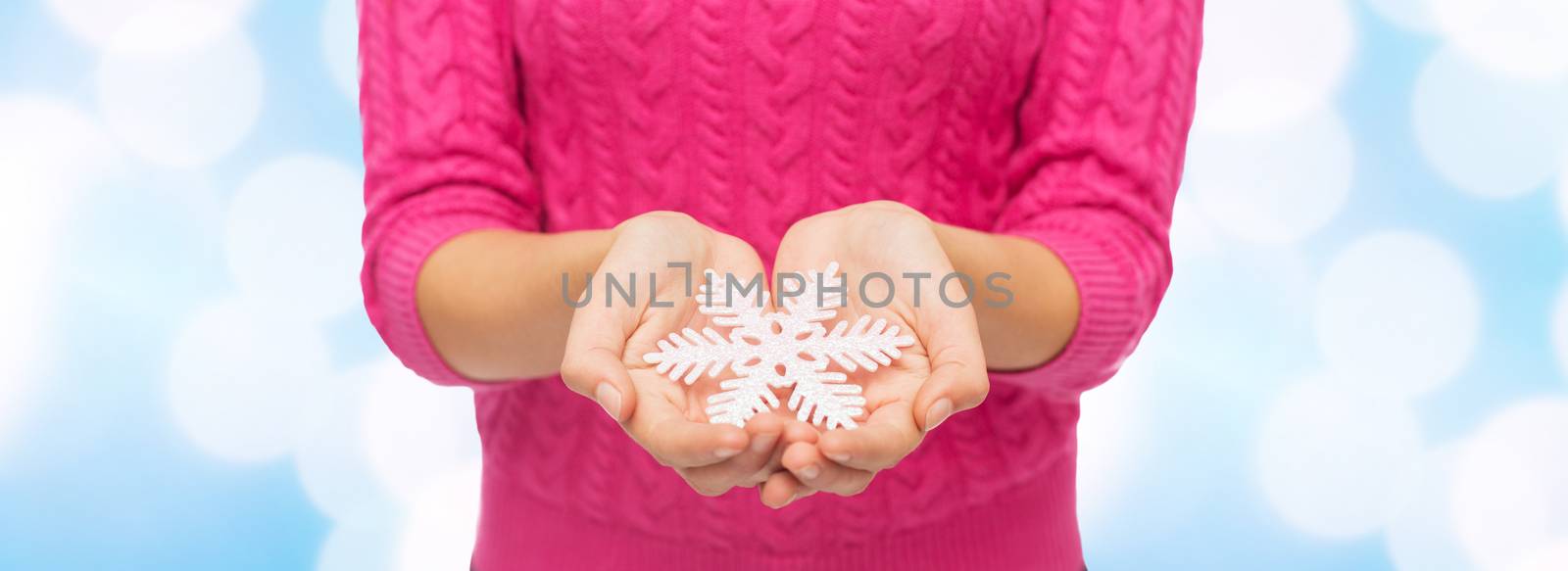 christmas, holidays and people concept - close up of woman in pink sweater holding snowflake over blue lights background