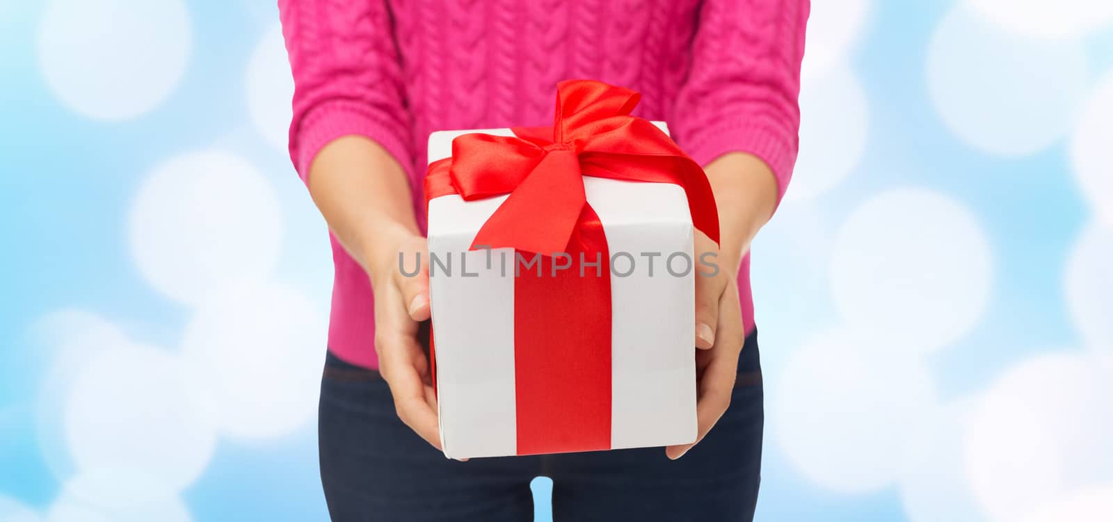 christmas, holidays and people concept - close up of woman in pink sweater holding gift box over blue lights background