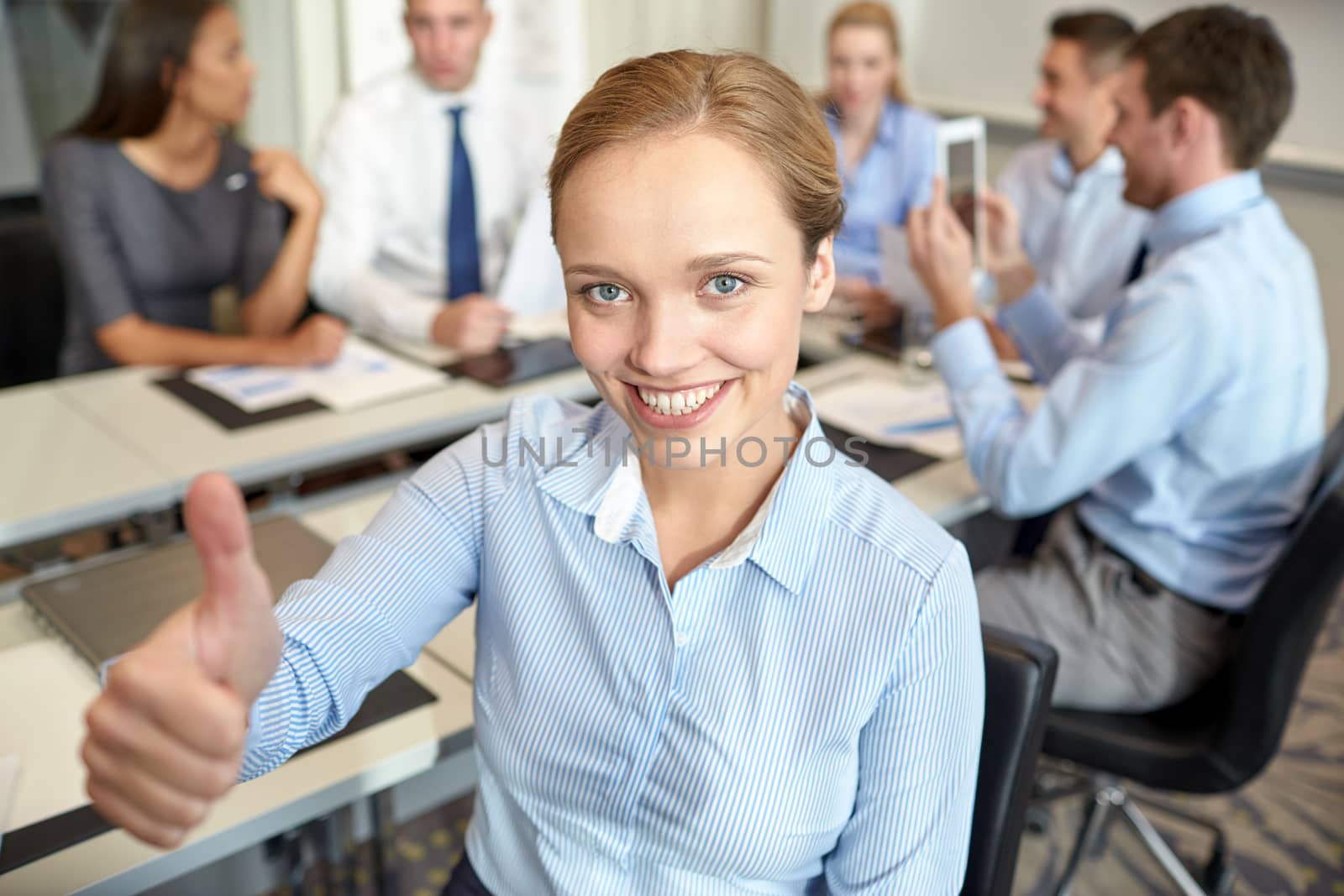 business, people, gesture and teamwork concept - smiling businesswoman showing thumbs up with group of businesspeople meeting in office