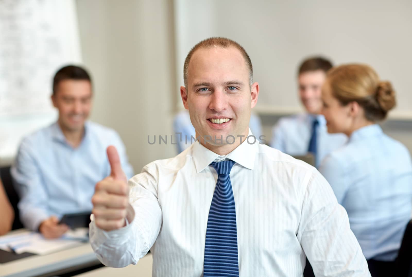 business, people, gesture and teamwork concept - smiling businessman showing thumbs up with group of businesspeople meeting in office