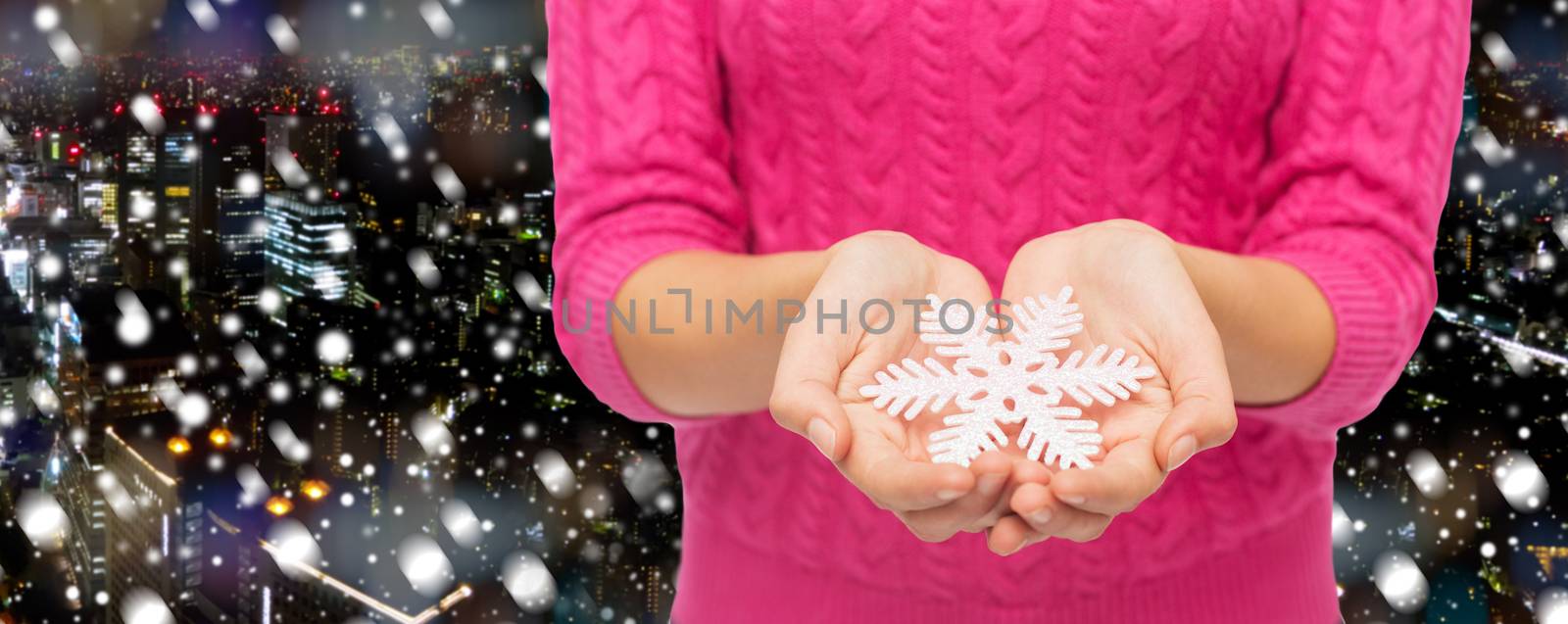 christmas, holidays and people concept - close up of woman in pink sweater holding snowflake over snowy night city background