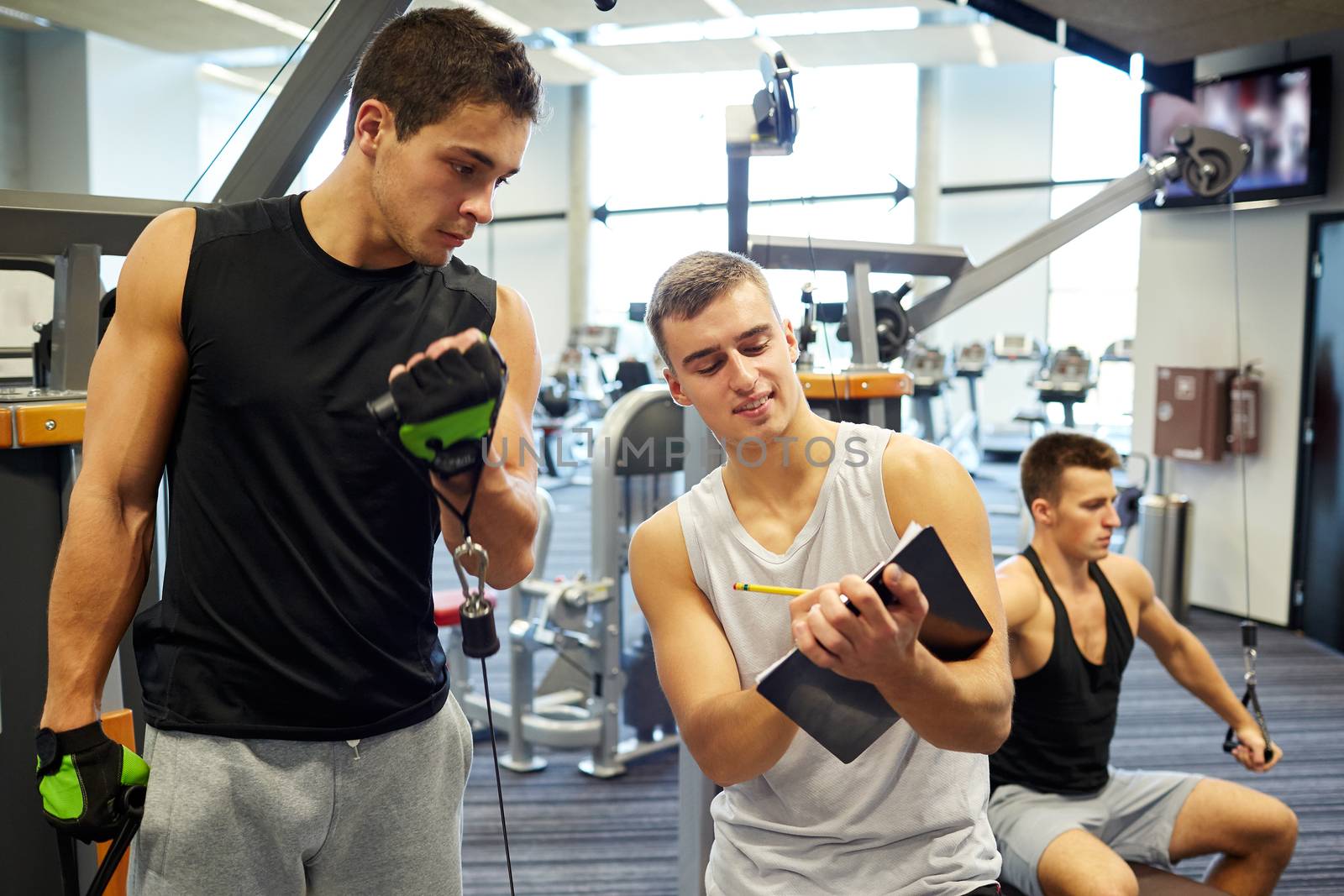 sport, fitness, lifestyle and people concept - men with clipboard taking notes and exercising on gym machine