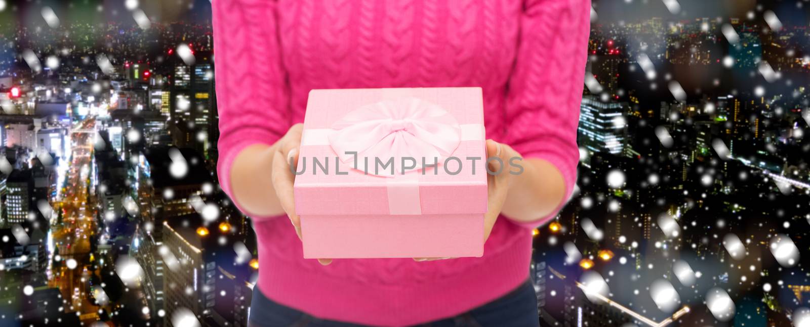 christmas, holidays and people concept - close up of woman in pink sweater holding gift box over snowy night city background