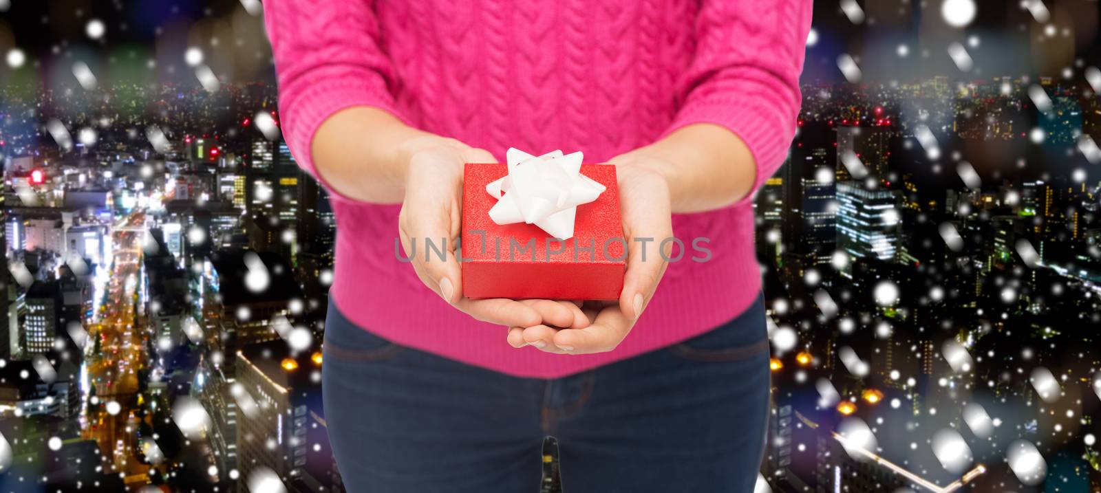 christmas, holidays and people concept - close up of woman in pink sweater holding gift box over snowy night city background