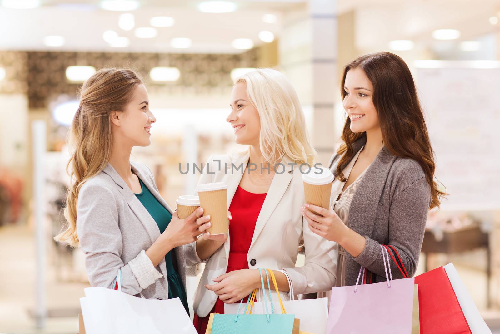 sale, consumerism and people concept - happy young women with shopping bags and coffee paper cup in mall