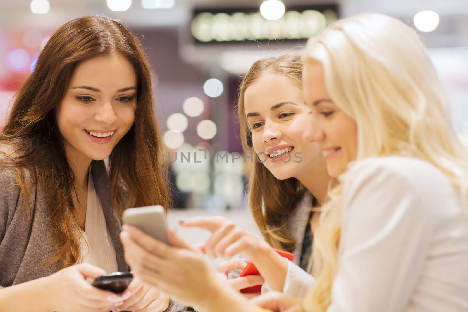 sale, consumerism, technology and people concept - happy young women with smartphones and tablet pc in mall or city