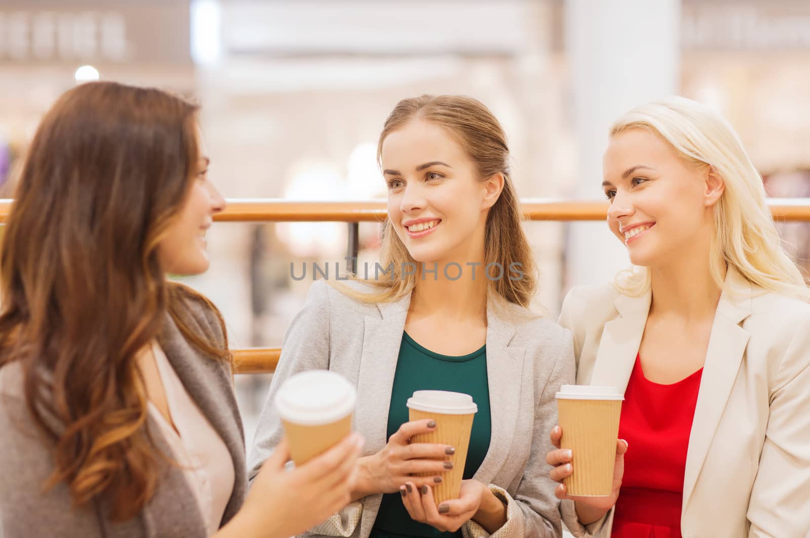 sale, consumerism and people concept - happy young women with shopping bags and coffee paper cups in mall