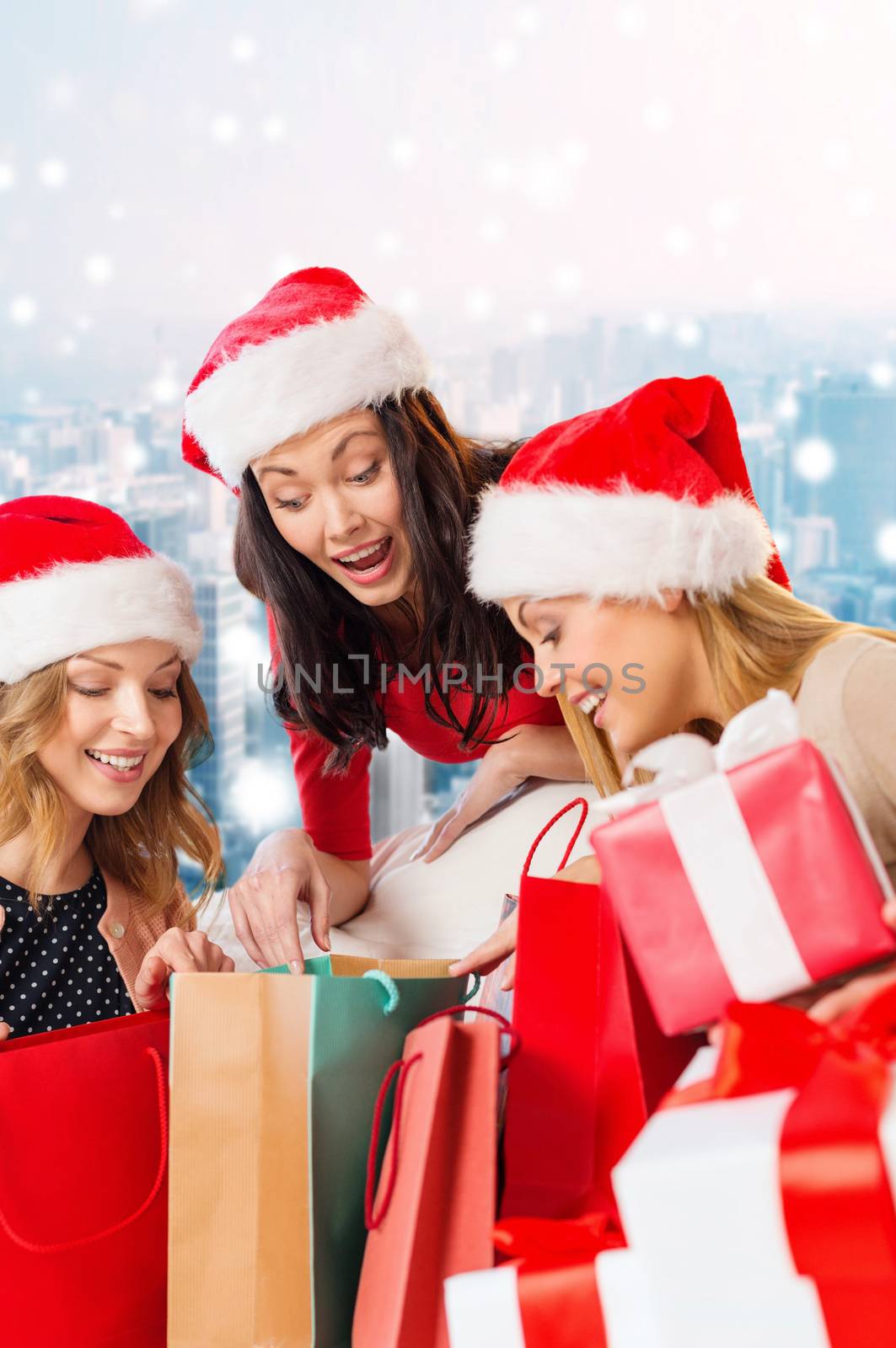 sale, winter holidays, christmas and people concept - smiling young women in santa helper hats with gifts and shopping bags over snowy city background