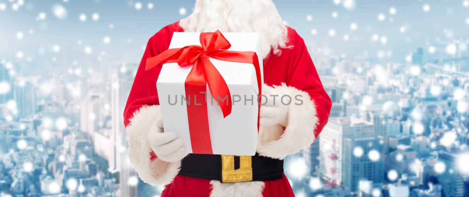 christmas, holidays and people concept - close up of santa claus with gift box over snowy city background