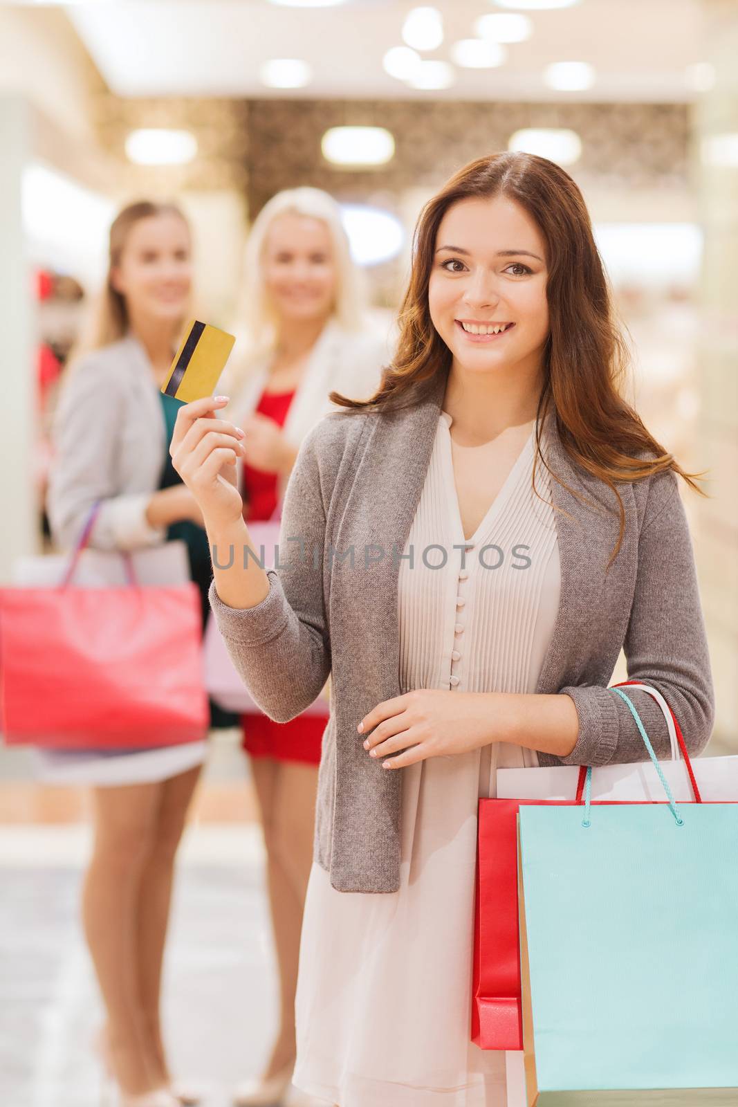 sale, consumerism, money and people concept - happy young women with shopping bags and credit card in mall