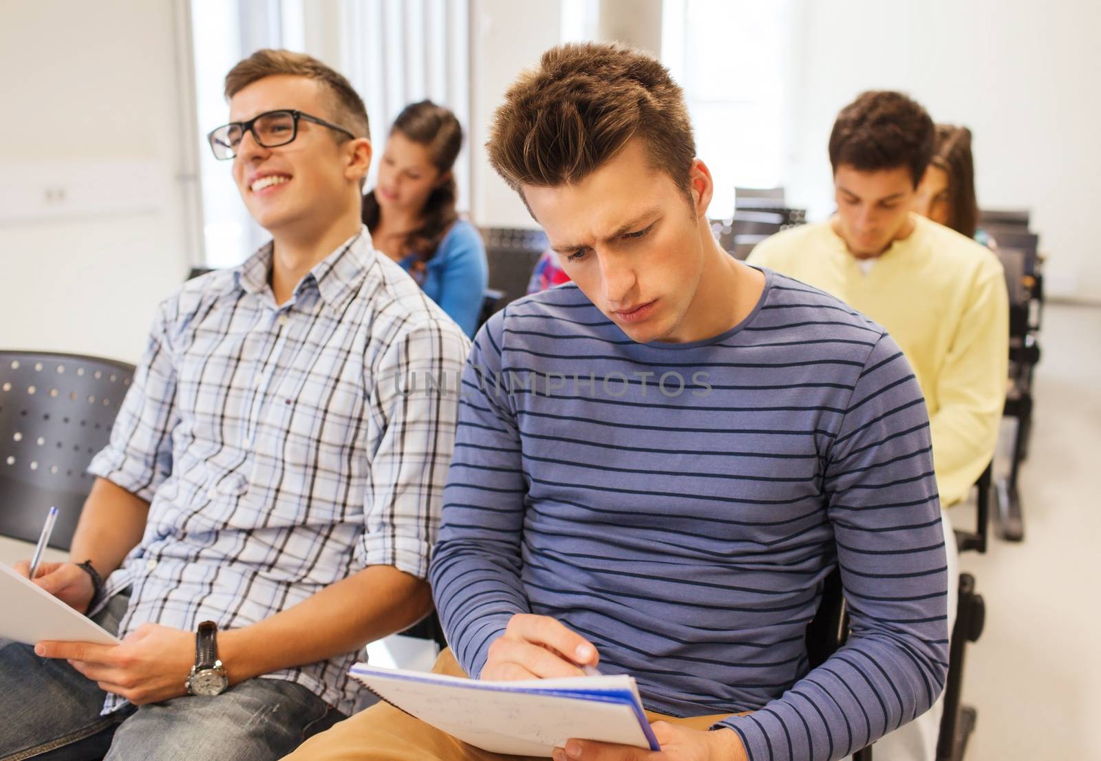 education, high school, teamwork and people concept - group of smiling students with notepads sitting in lecture hall