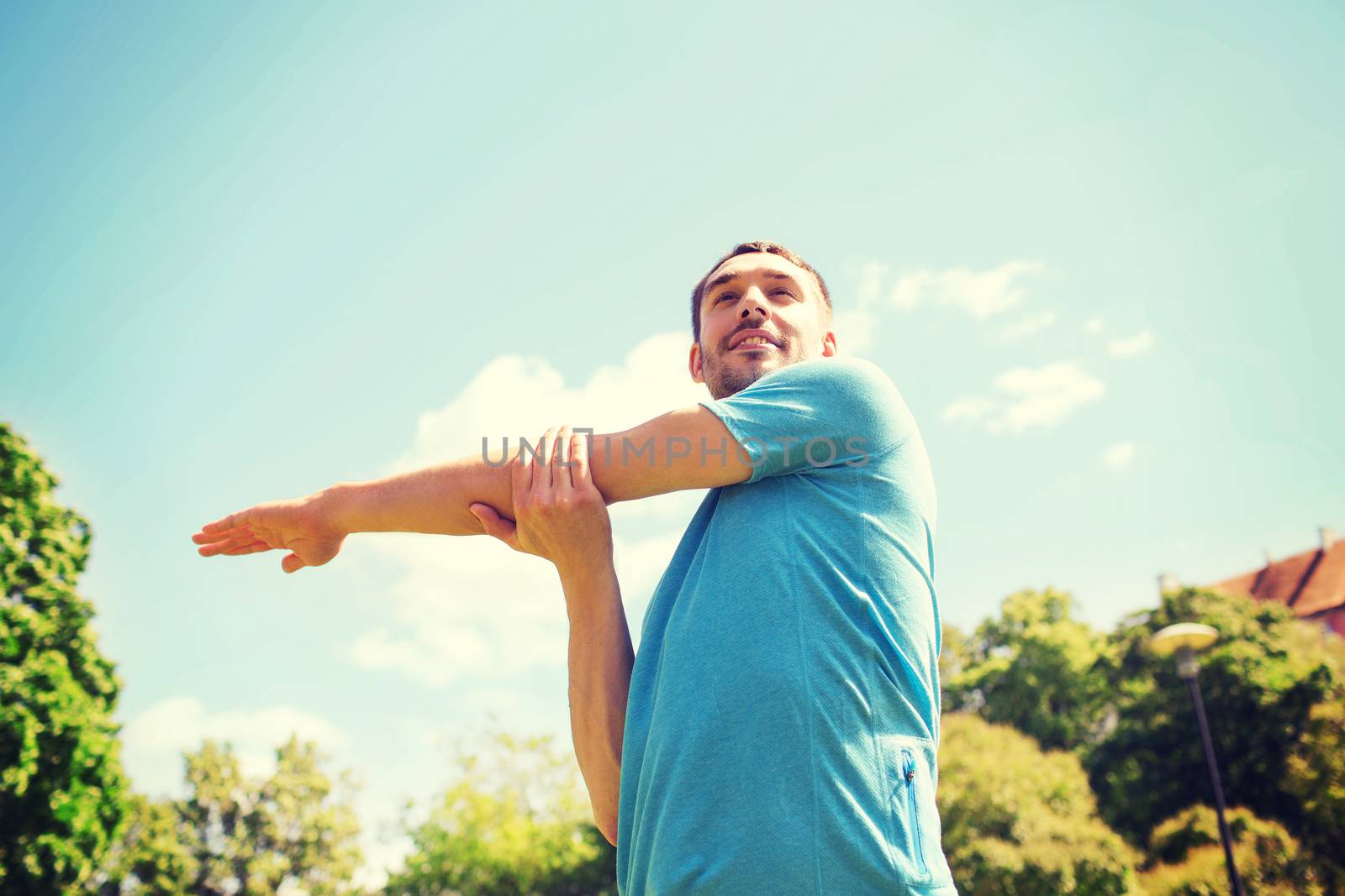 fitness, sport, training and lifestyle concept - smiling man stretching hand outdoors