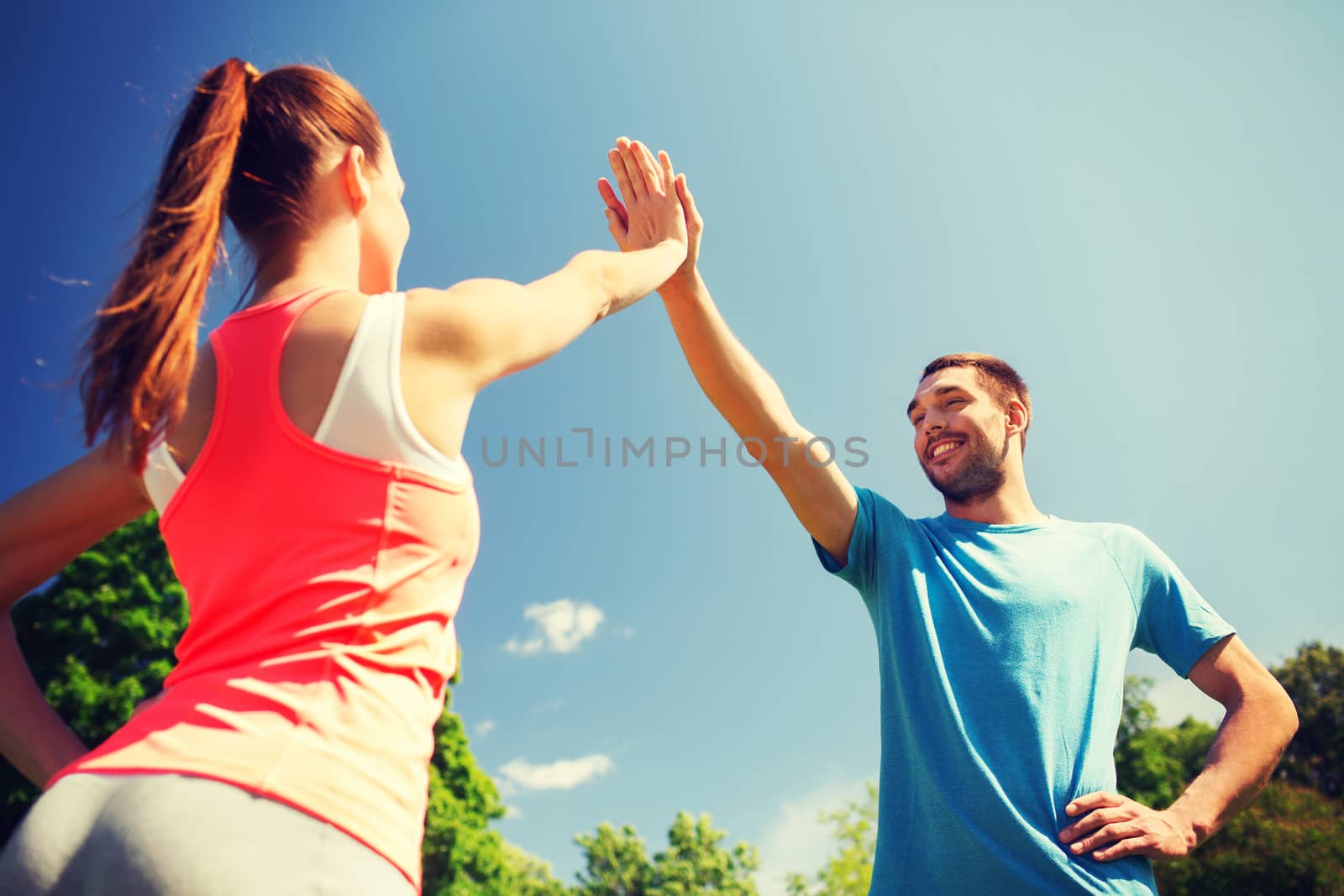 two smiling people making high five outdoors by dolgachov