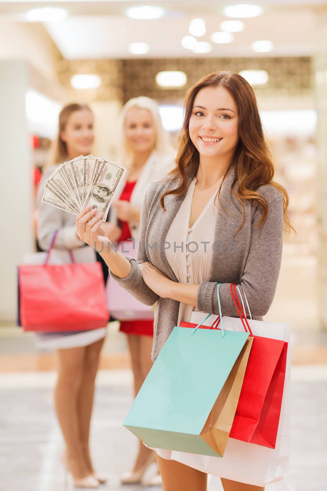 sale, consumerism and people concept - happy young women with shopping bags and dollar cash money in mall