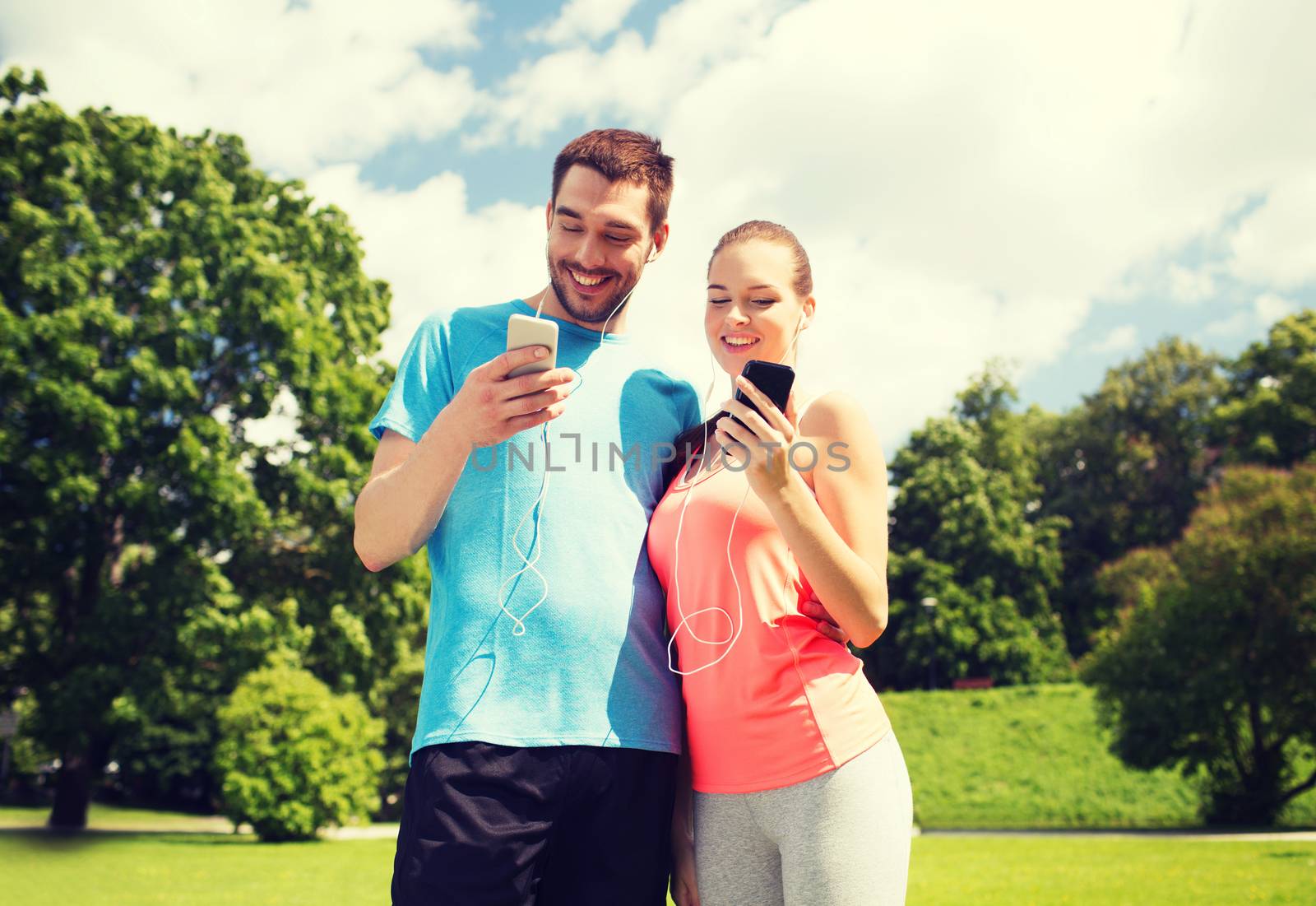 two smiling people with smartphones outdoors by dolgachov