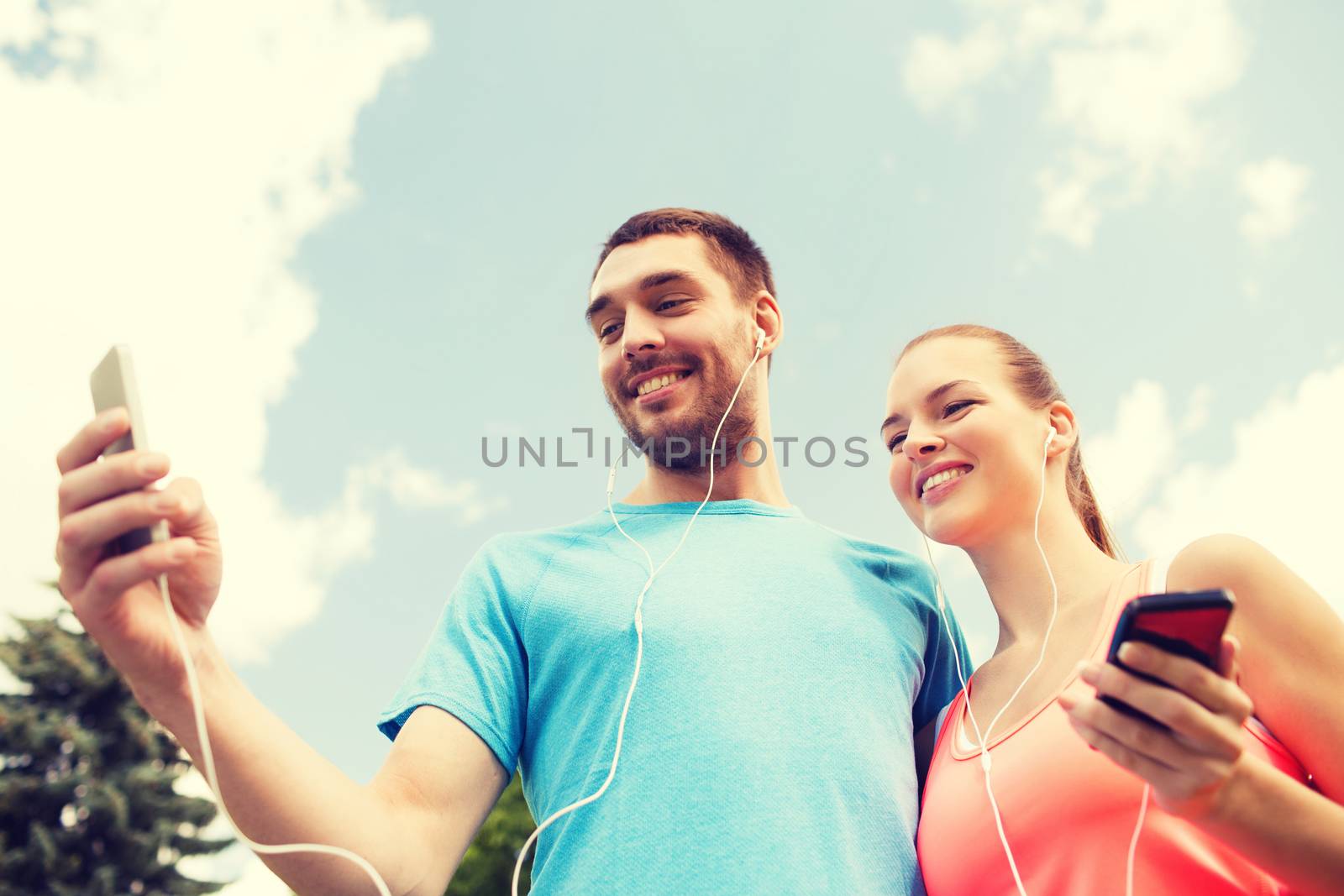 fitness, sport, training, technology and lifestyle concept - two smiling people with smartphones and earphones outdoors