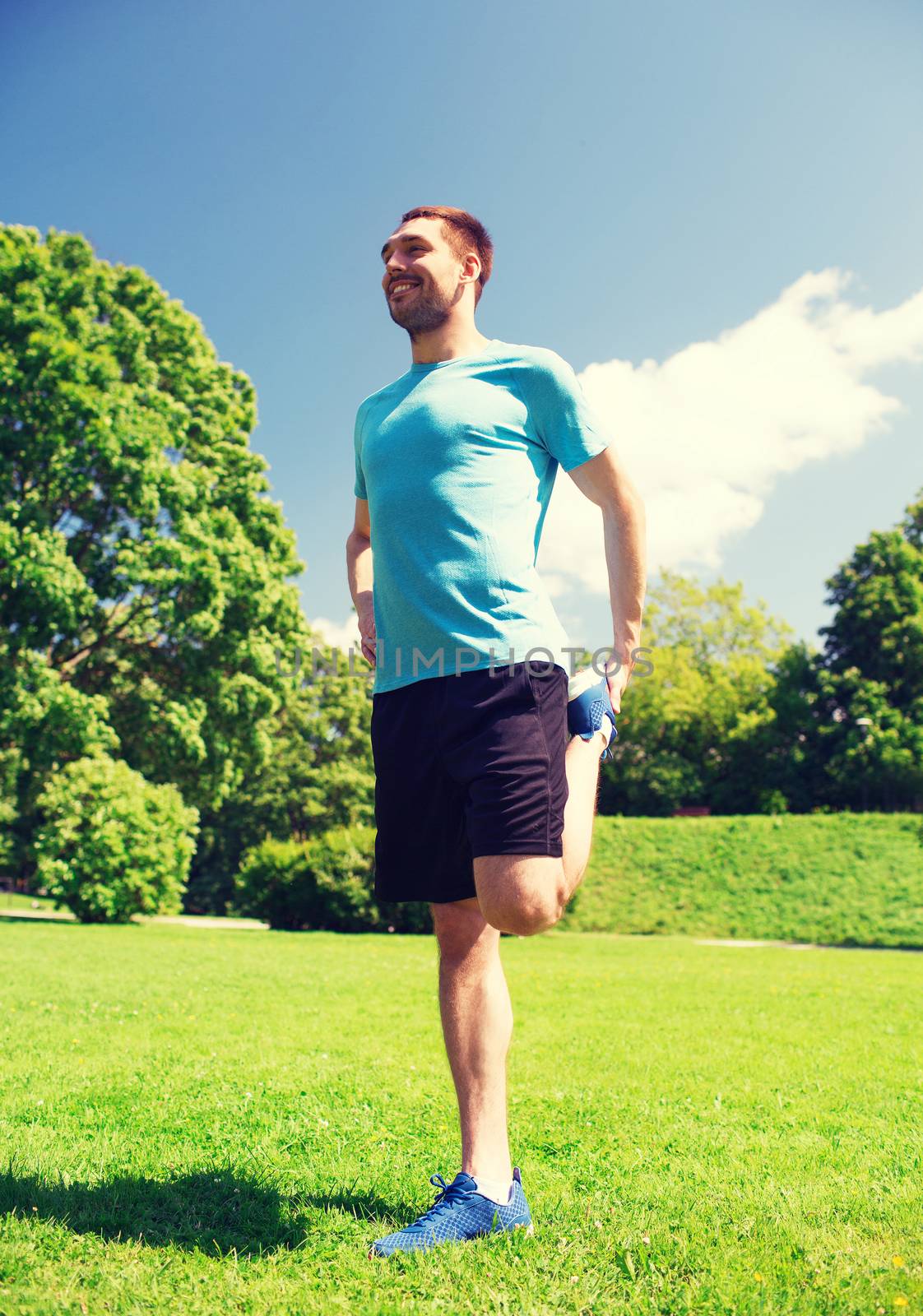 fitness, sport, training and lifestyle concept - smiling man stretching leg outdoors