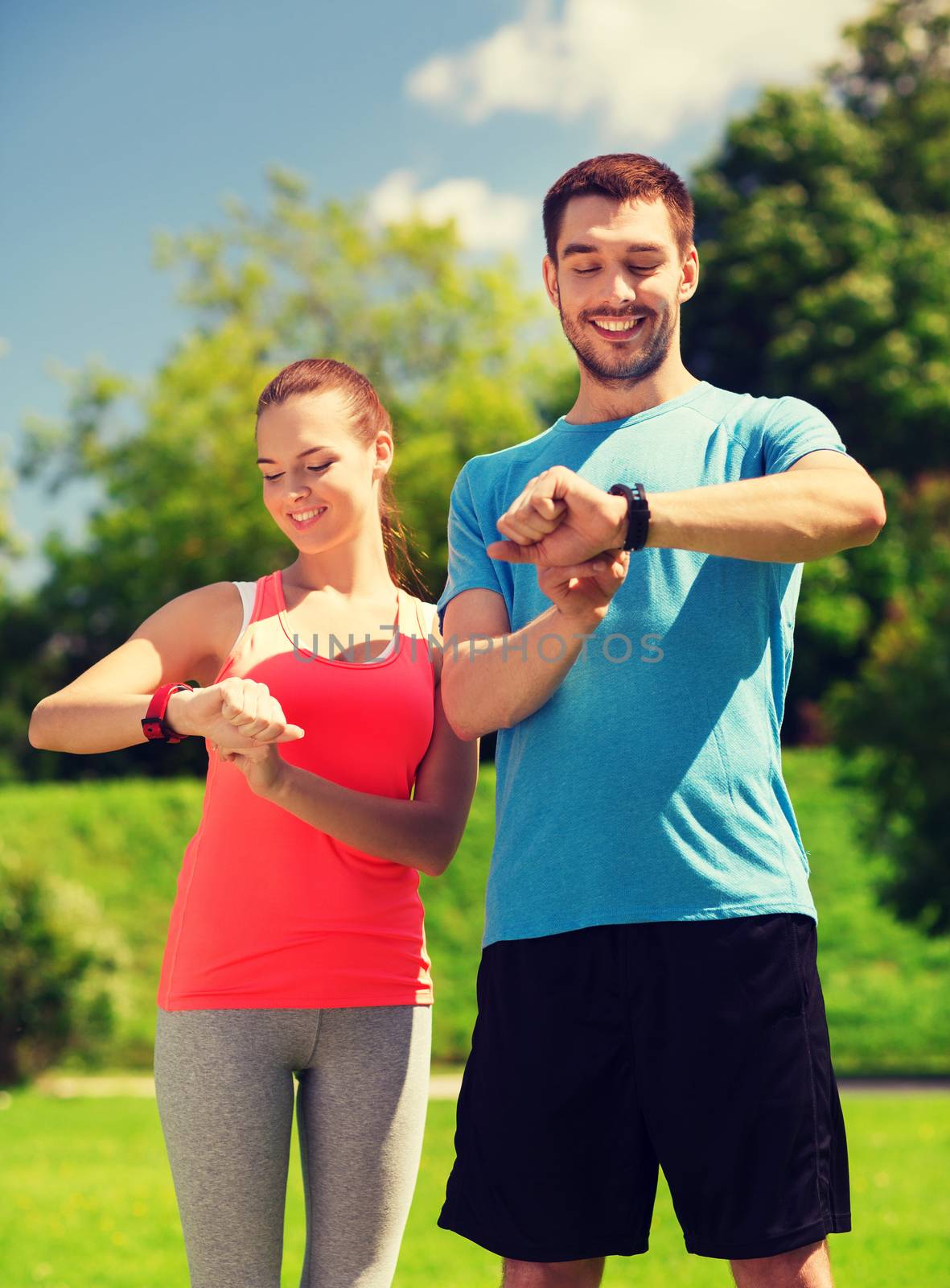 fitness, sport, training, technology and lifestyle concept - two smiling people with heart rate watches outdoors