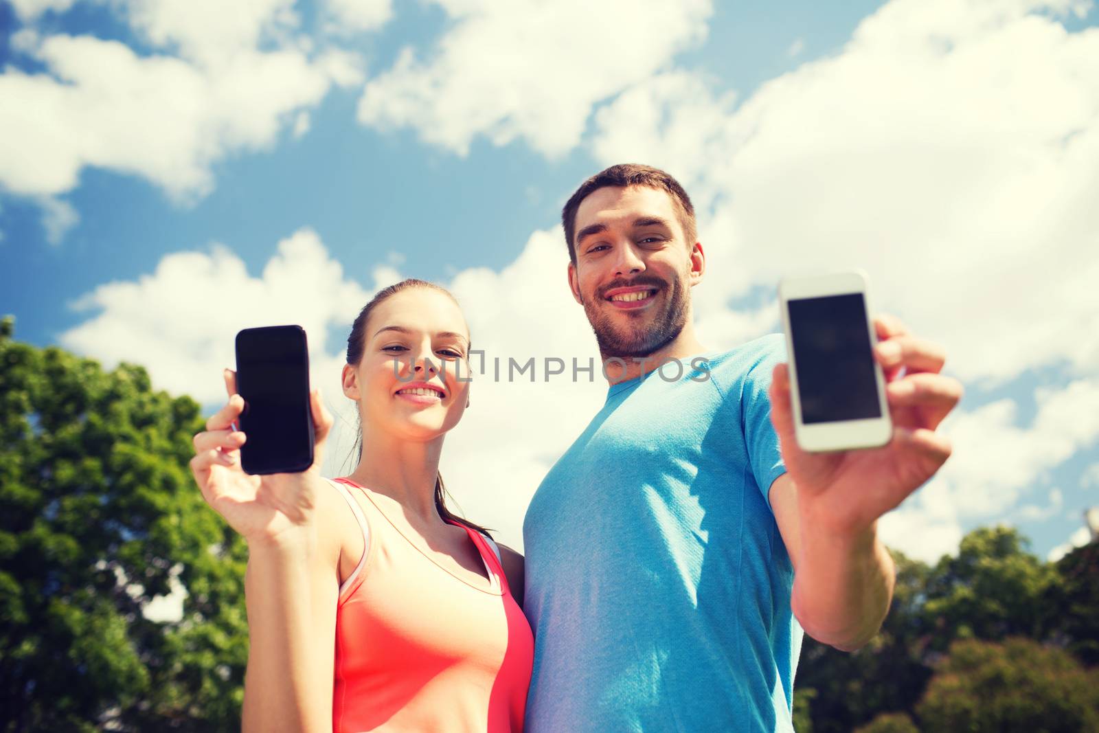 fitness, sport, training, technology and lifestyle concept - two smiling people with smartphones outdoors