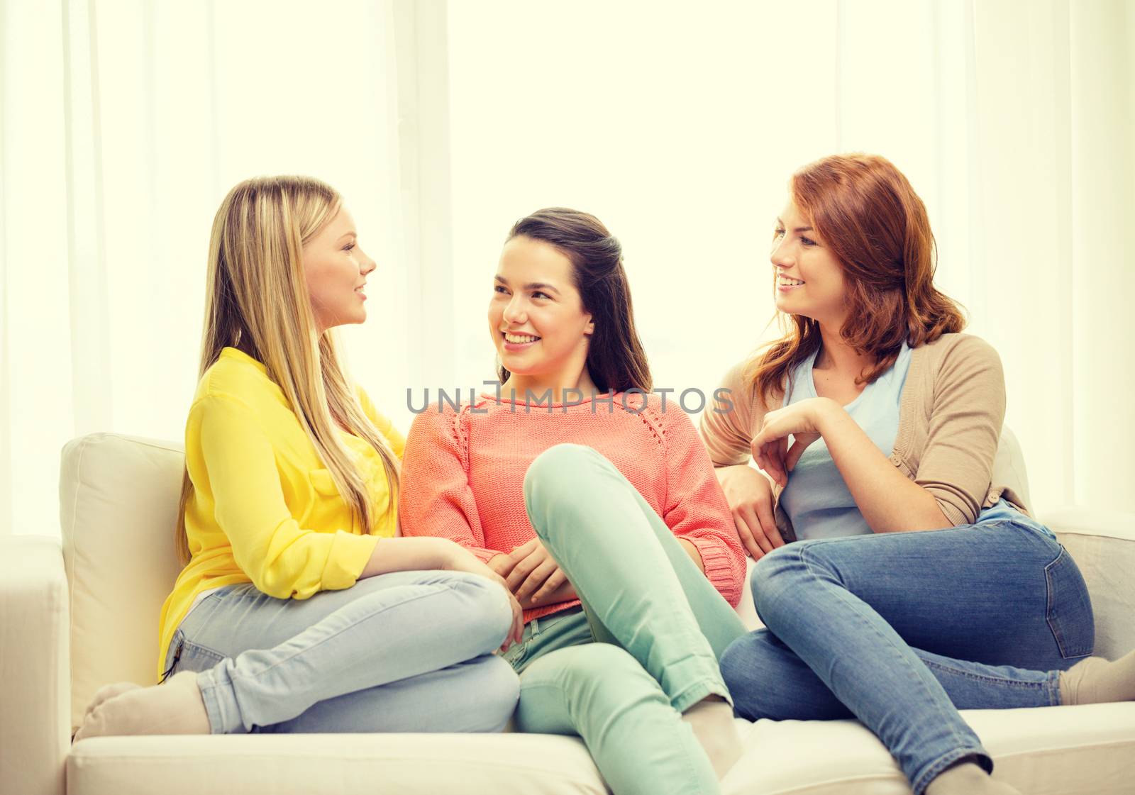 friendship and happiness concept - three girlfriends having a talk at home