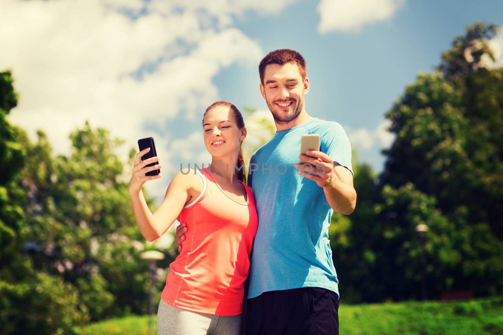 two smiling people with smartphones outdoors by dolgachov