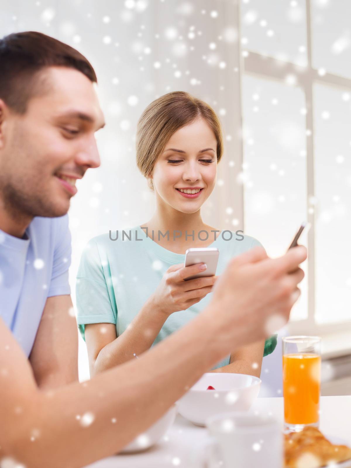 smiling couple with smartphones having breakfast by dolgachov