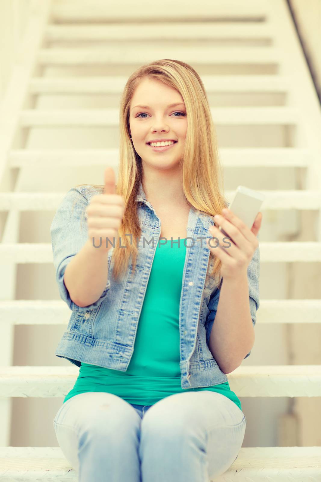 education and technology concept - smiling female student with smartphone sitting on staircase and showing thumbs up