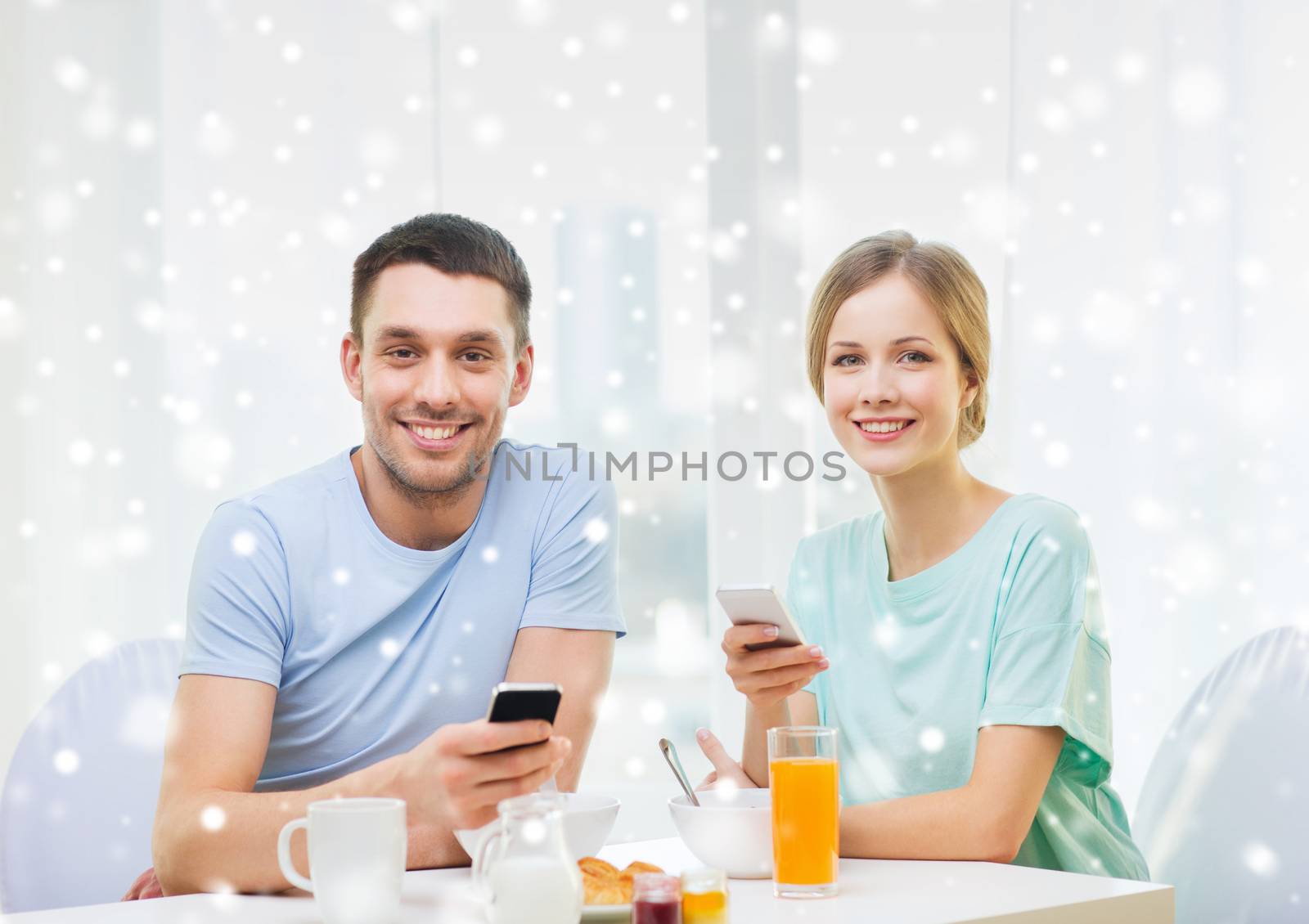 smiling couple with smartphones having breakfast by dolgachov
