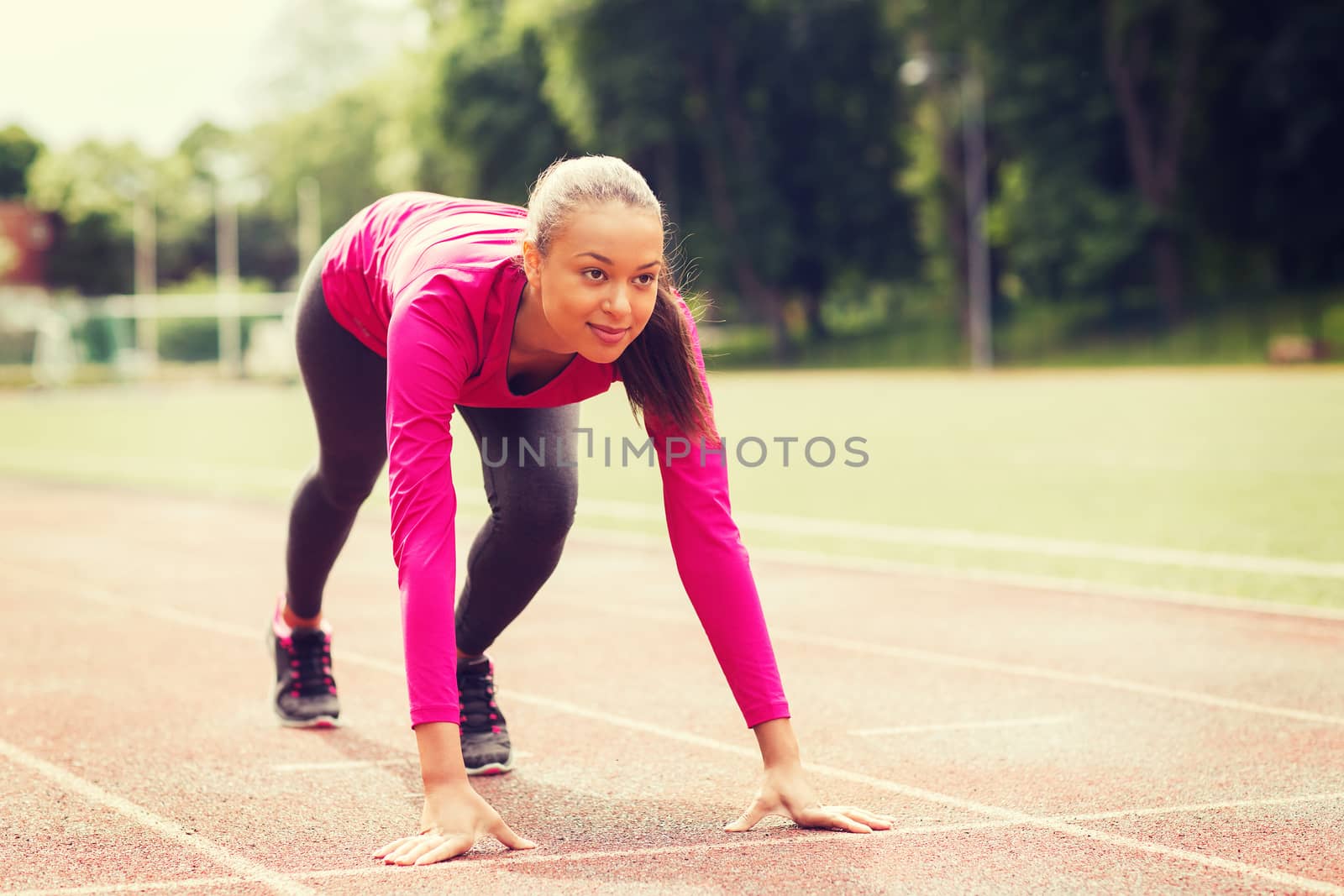 fitness, sport, training and lifestyle concept - smiling african american woman running on track outdoors