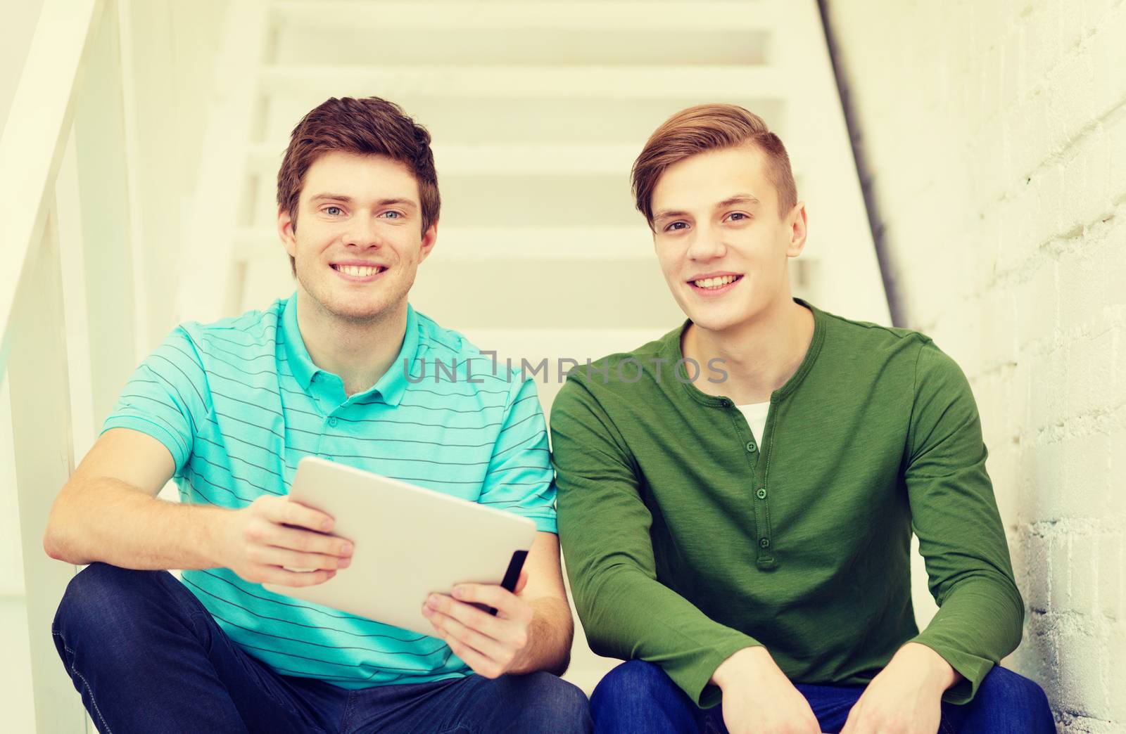 education and technology concept - smiling male students with tablet pc computer sitting on staircase