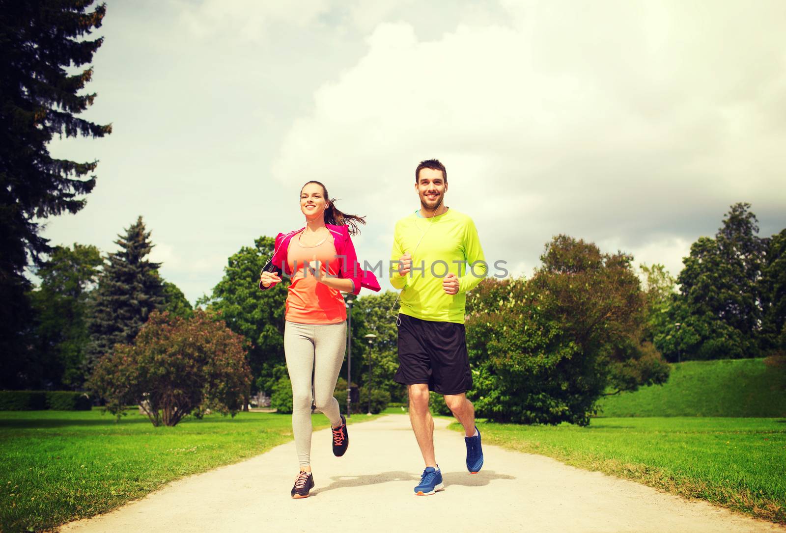 smiling couple with earphones running outdoors by dolgachov