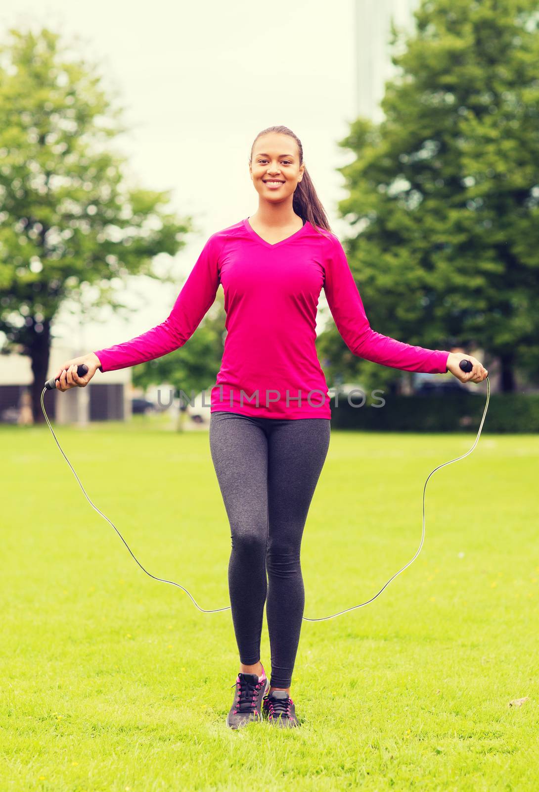 smiling woman exercising with jump-rope outdoors by dolgachov