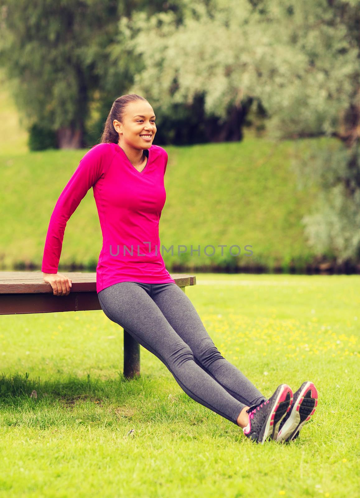 fitness, sport, training, park and lifestyle concept - smiling african american woman doing push-ups on bench outdoors