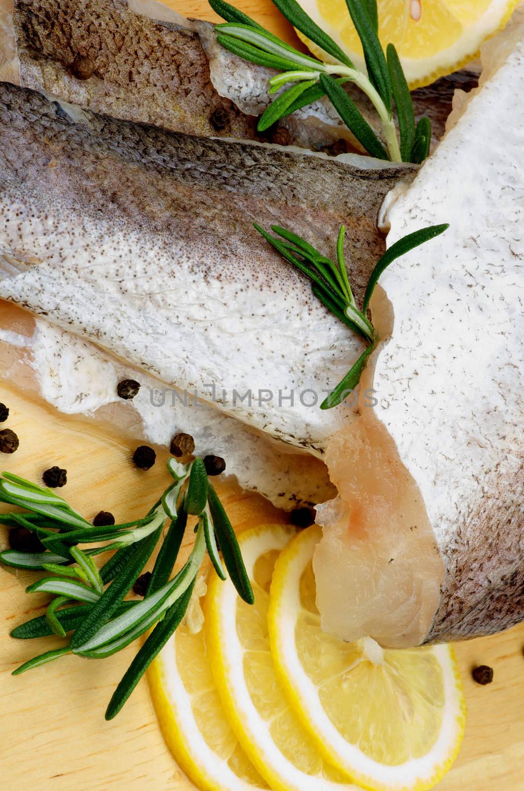 Raw Fillet of Fish Hake with Lemon, Rosemary and Black Peppercorn closeup on Wooden Cutting Board