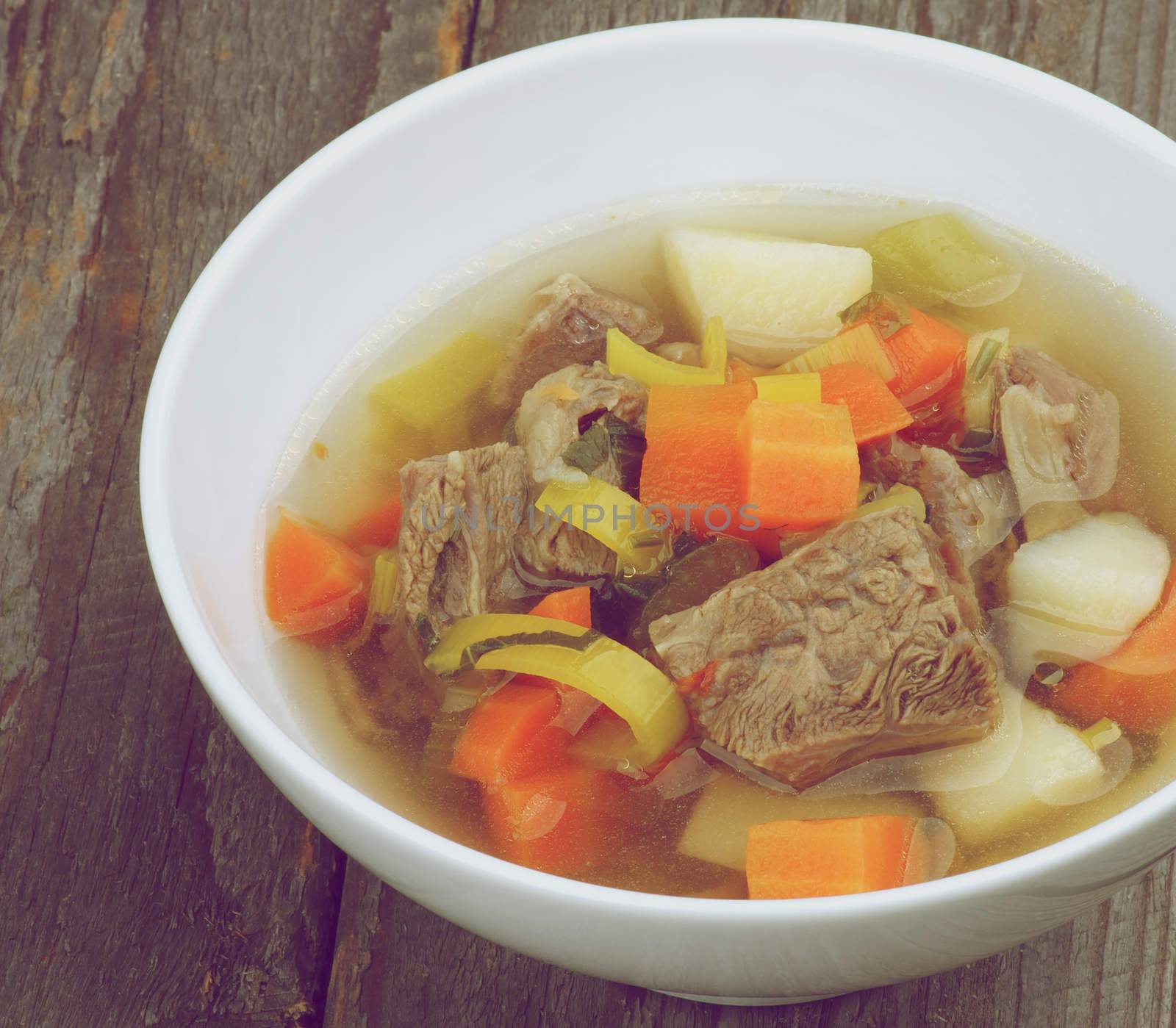 Rustic Beef Soup with Potato, Carrot, Leek and Greens in White Bowl Cross Section on Wooden background. Retro Styled