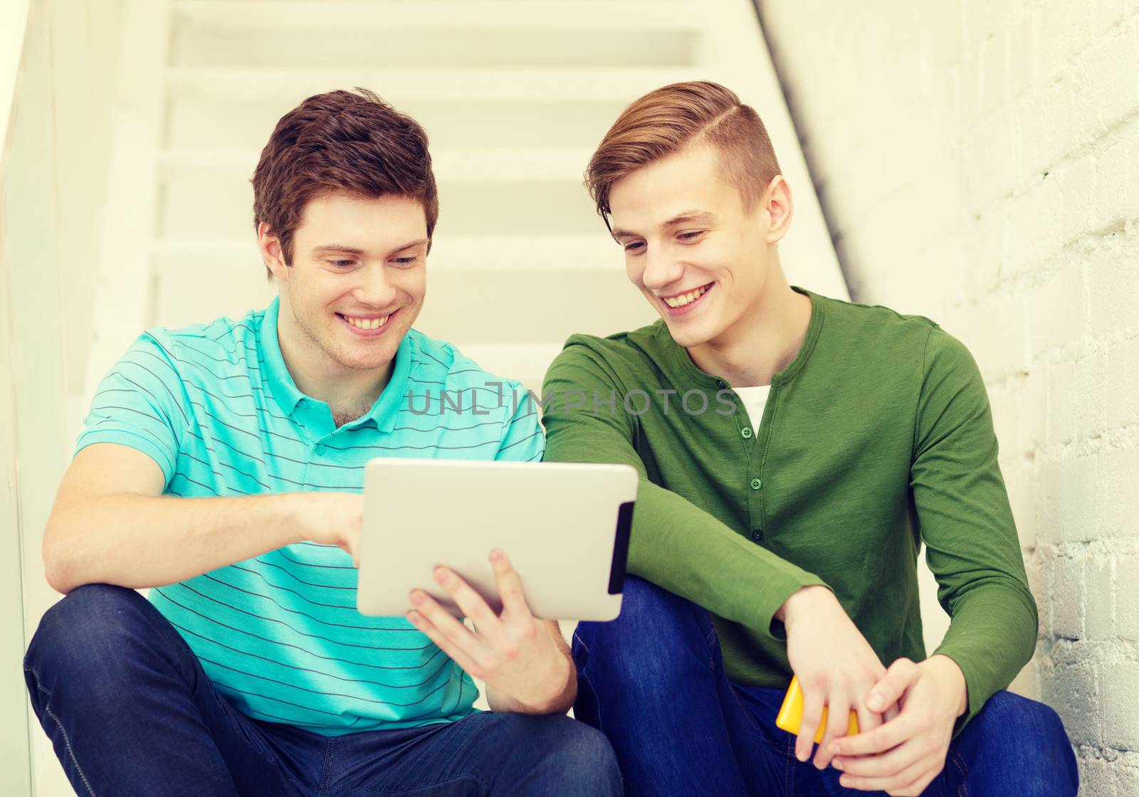 education and technology concept - smiling male students with tablet pc computer sitting on staircase