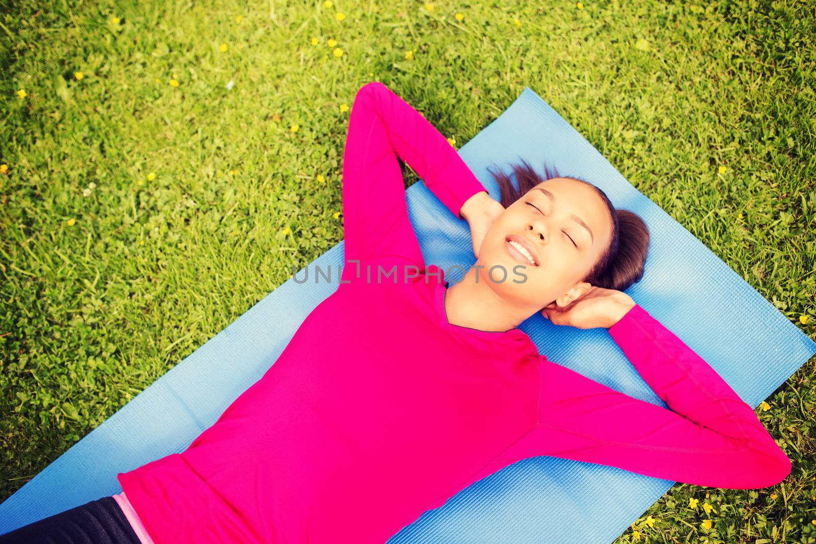 fitness, sport, training, park and lifestyle concept - smiling african american woman doing exercises lying on mat outdoors