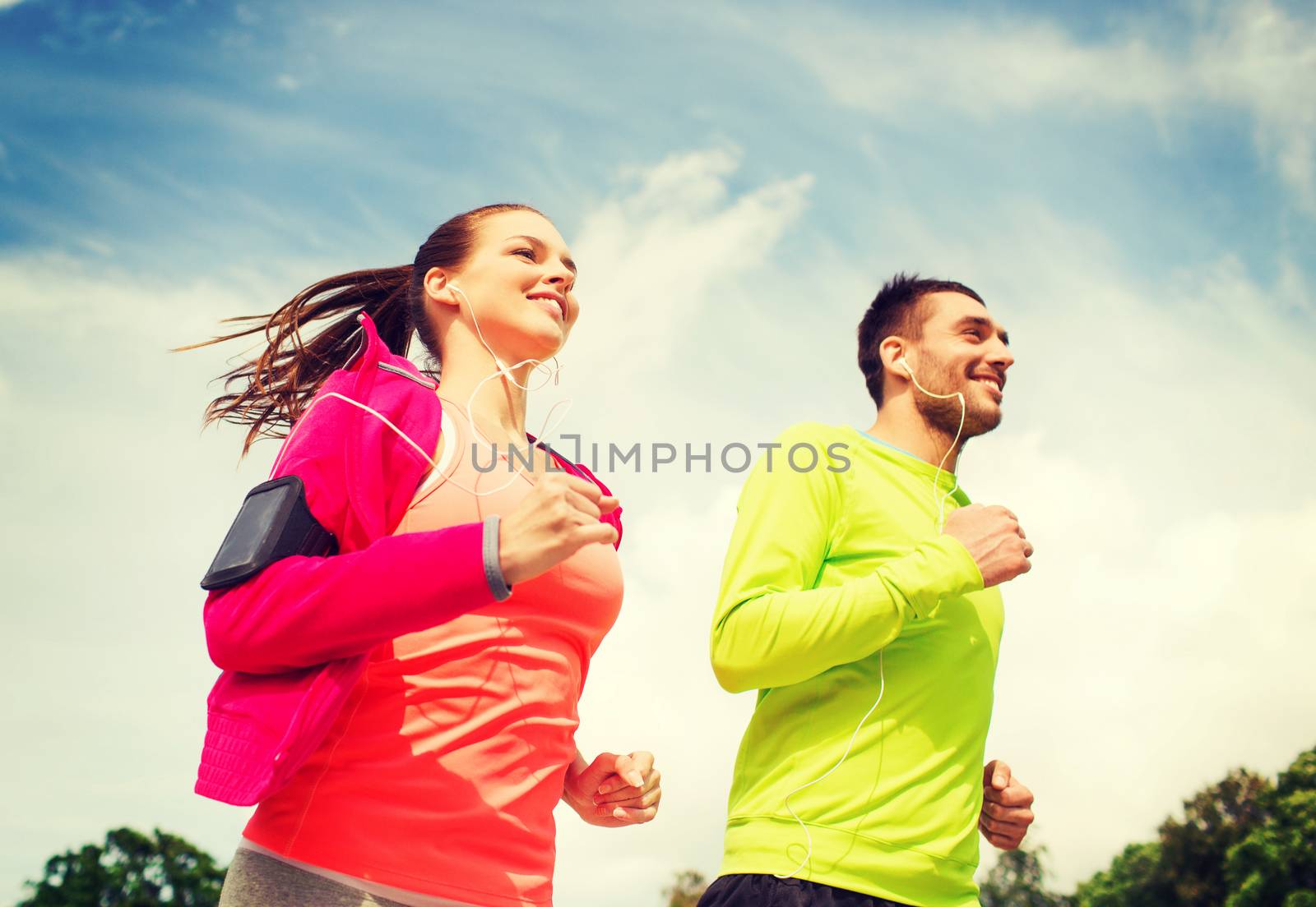 smiling couple with earphones running outdoors by dolgachov