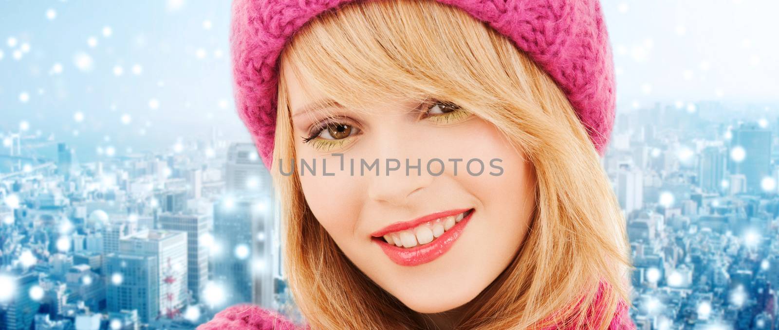 happiness, winter holidays, christmas and people concept - close up of smiling young woman in pink hat and scarf over blue snowy background