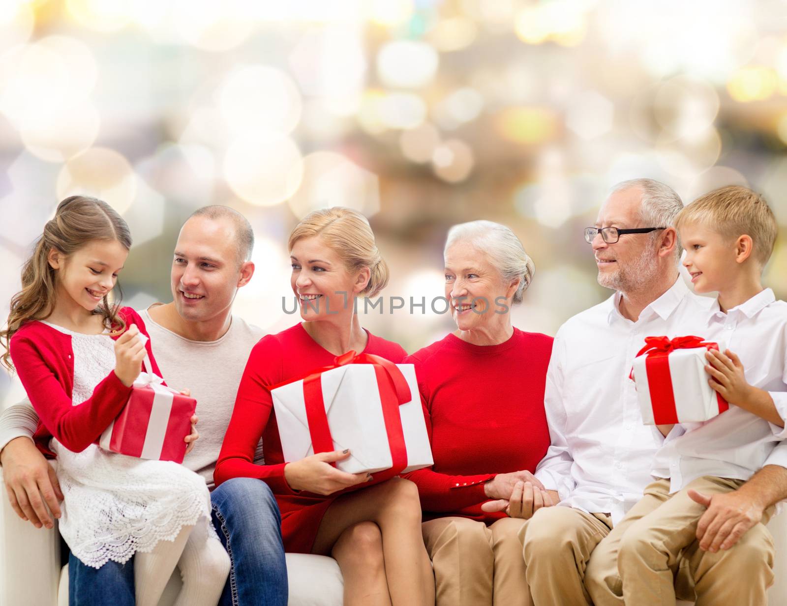 family, holidays, generation, christmas and people concept - smiling family with gift boxes sitting on couch over lights background