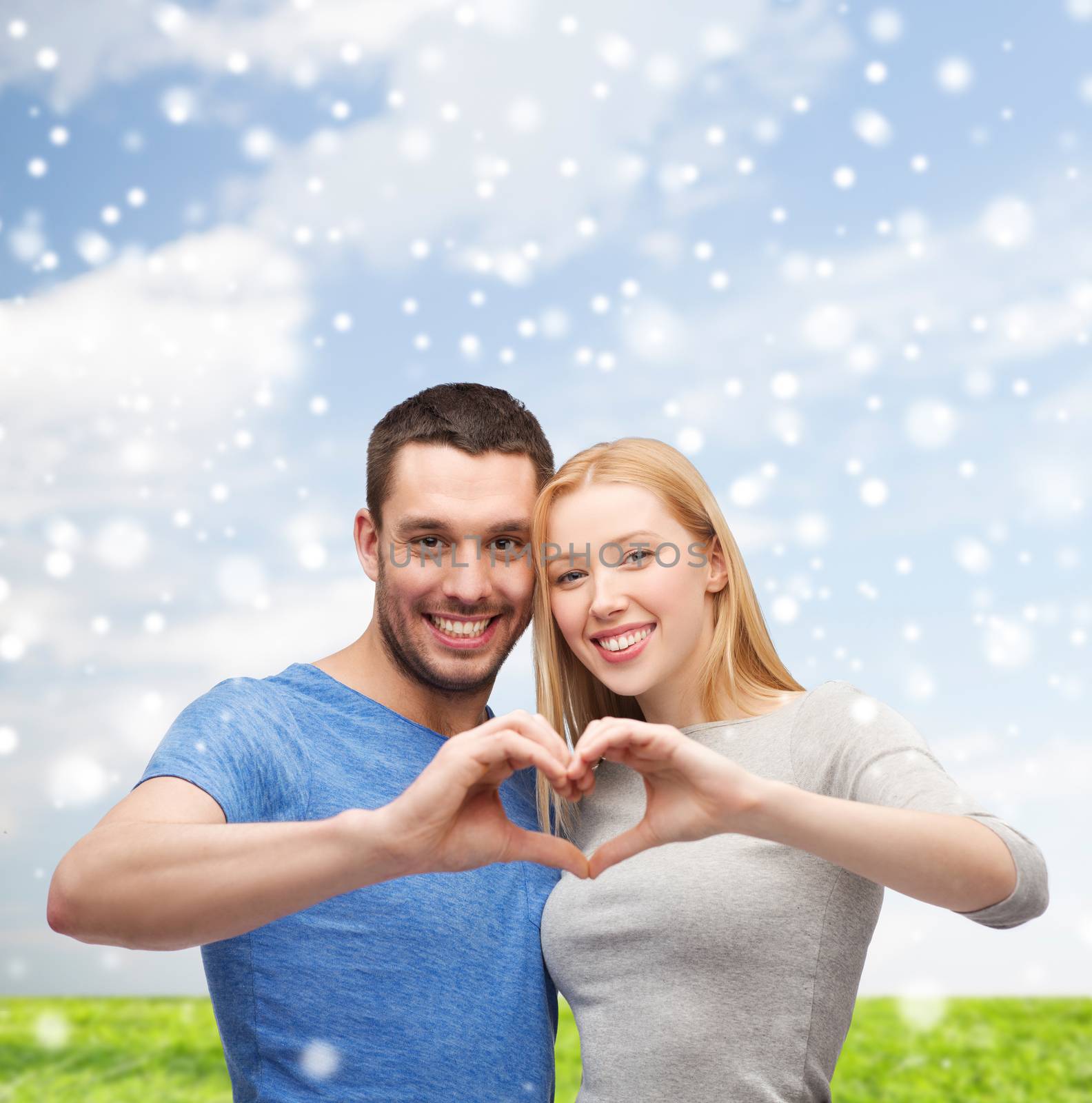 love, people and family concept - smiling couple making heart shape gesture hugging over blue sky, snow and grass background