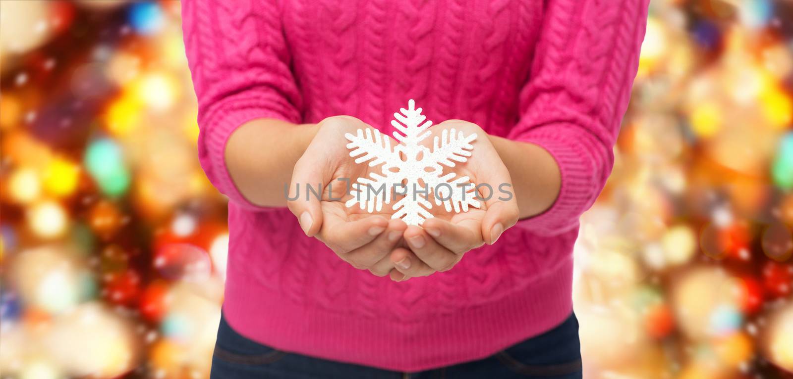 christmas, holidays and people concept - close up of woman in pink sweater holding snowflake decoration over red lights background