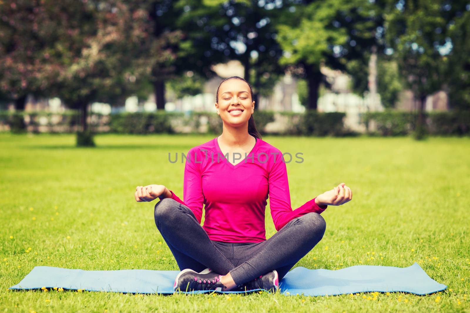 sport, meditation, park and lifestyle concept - smiling woman meditating on mat outdoors